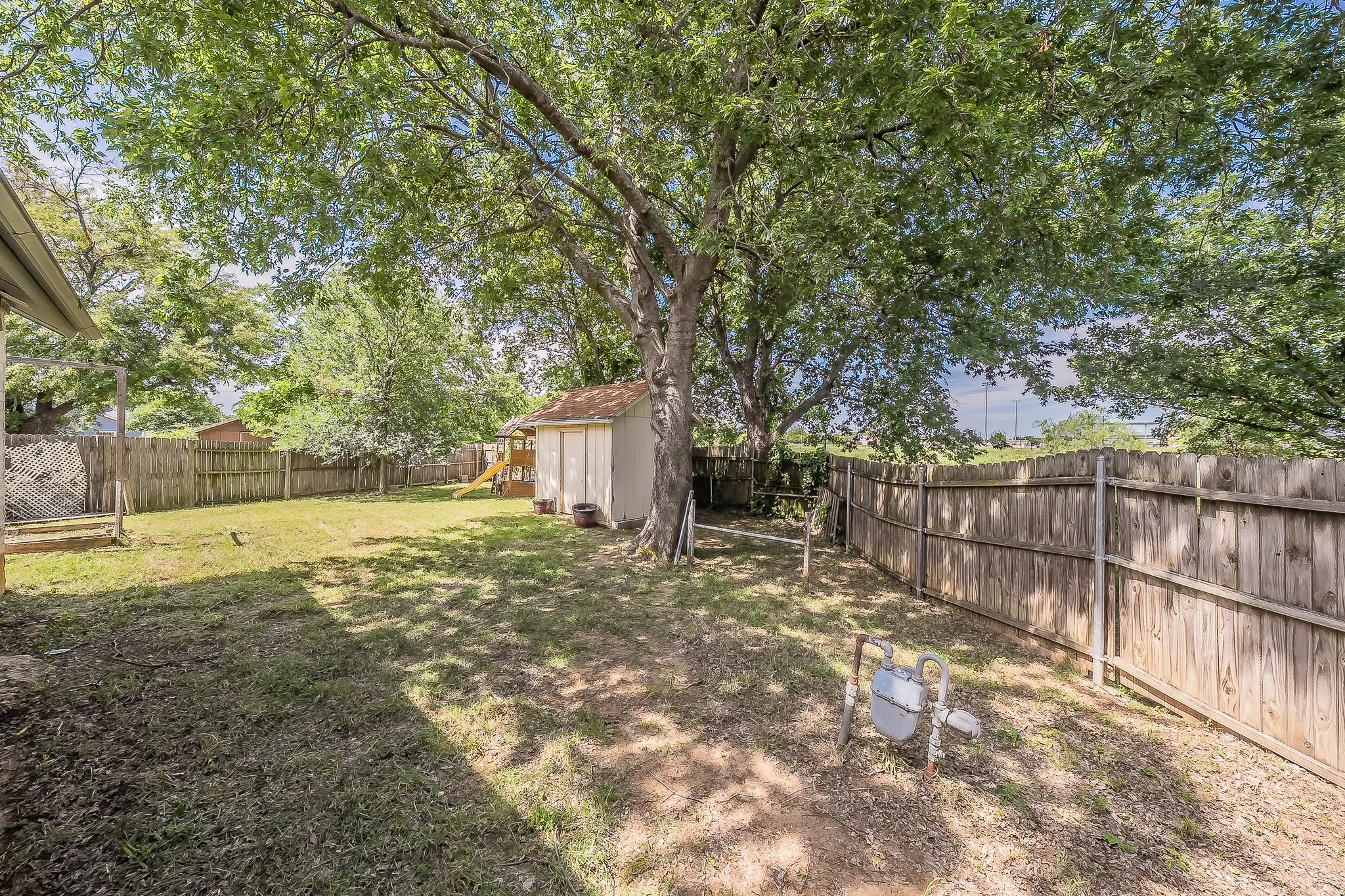Expansive backyard featuring a mature shade tree, privacy fencing, and a detached storage shed