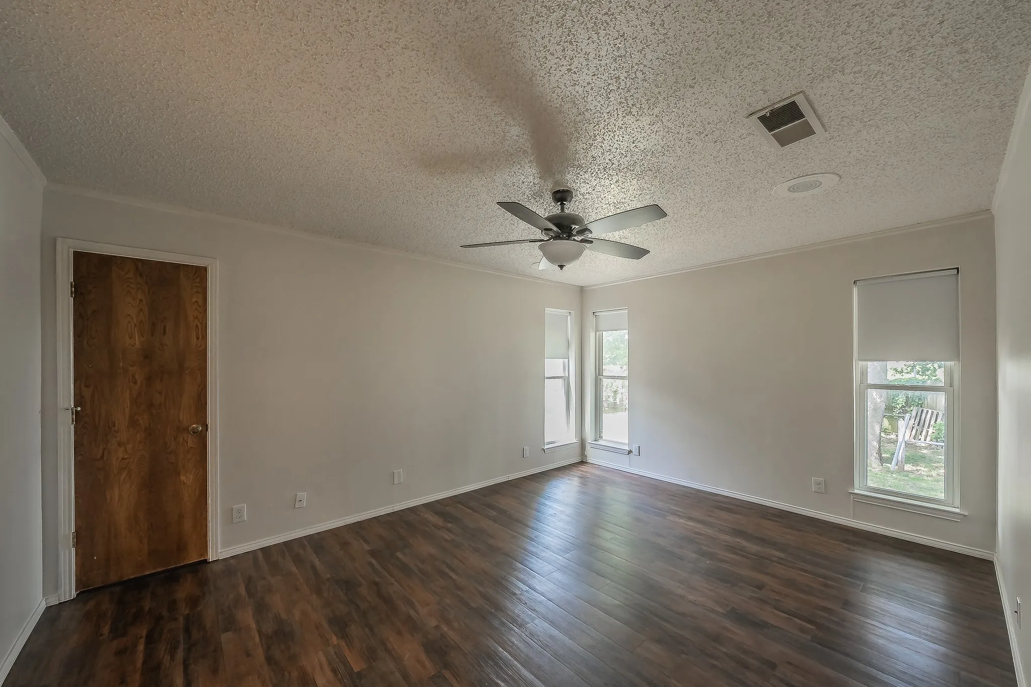 Spacious room featuring wood-finish flooring, light neutral walls, and a ceiling fan with integrated lighting