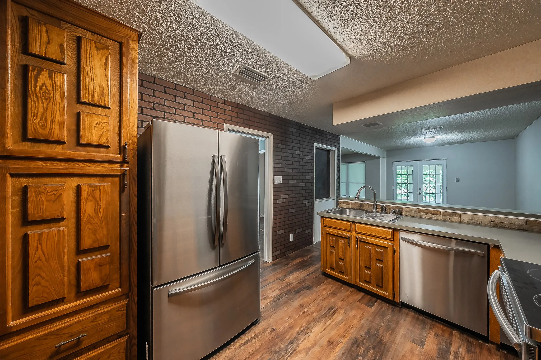 Kitchen featuring wood-finish flooring, dark brick accent wall, and built-in wood cabinetry