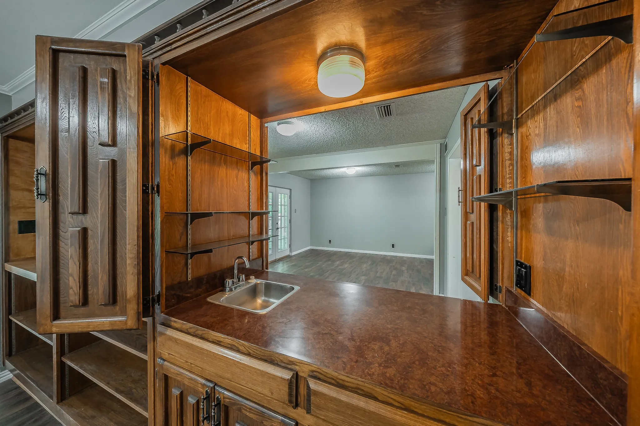 Built-in wet bar with a stainless steel sink, solid surface countertop, and wood cabinetry