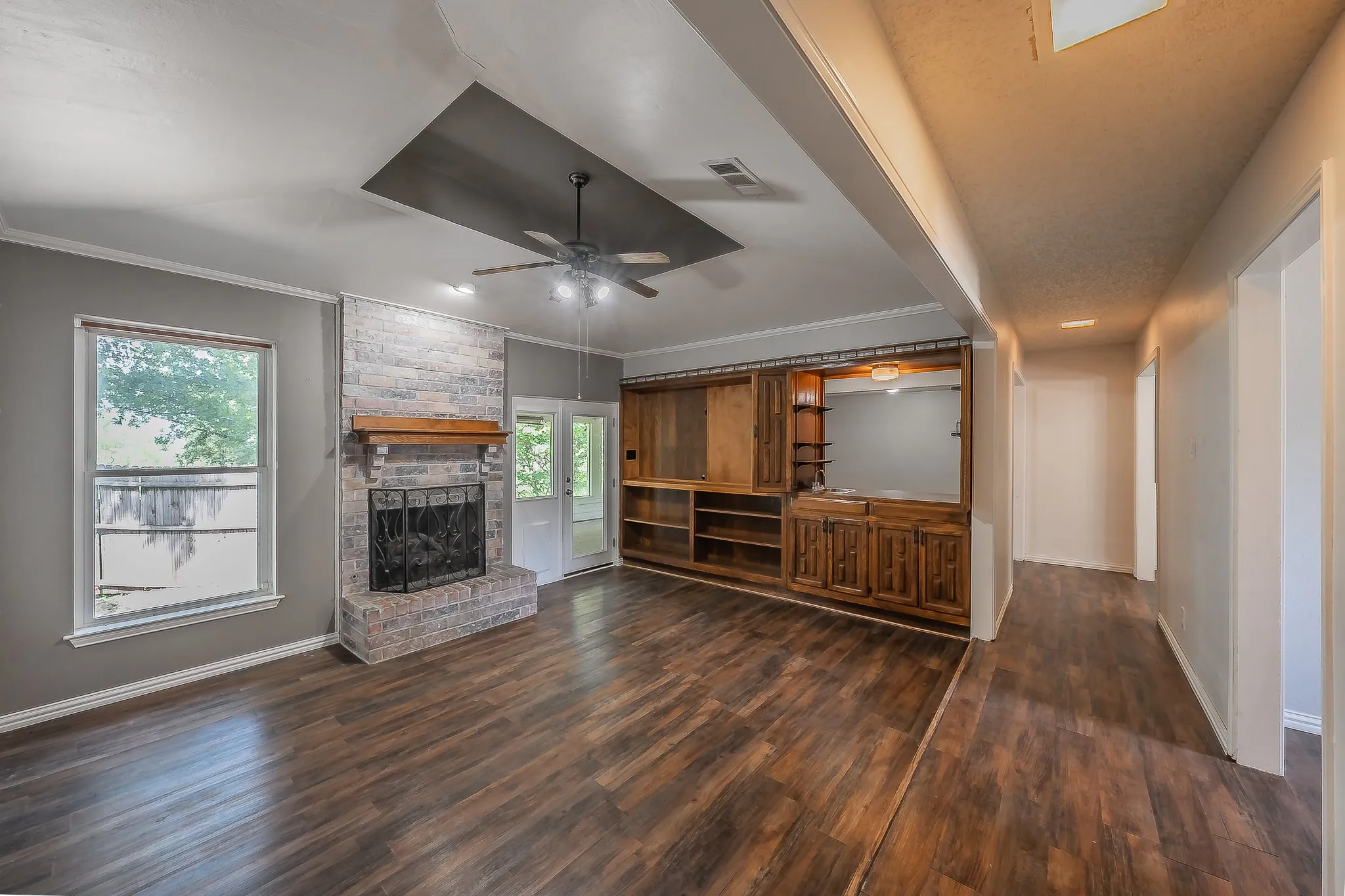 Spacious living area featuring wood-finish flooring, a brick fireplace with wood mantle, and a built-in entertainment center with cabinetry