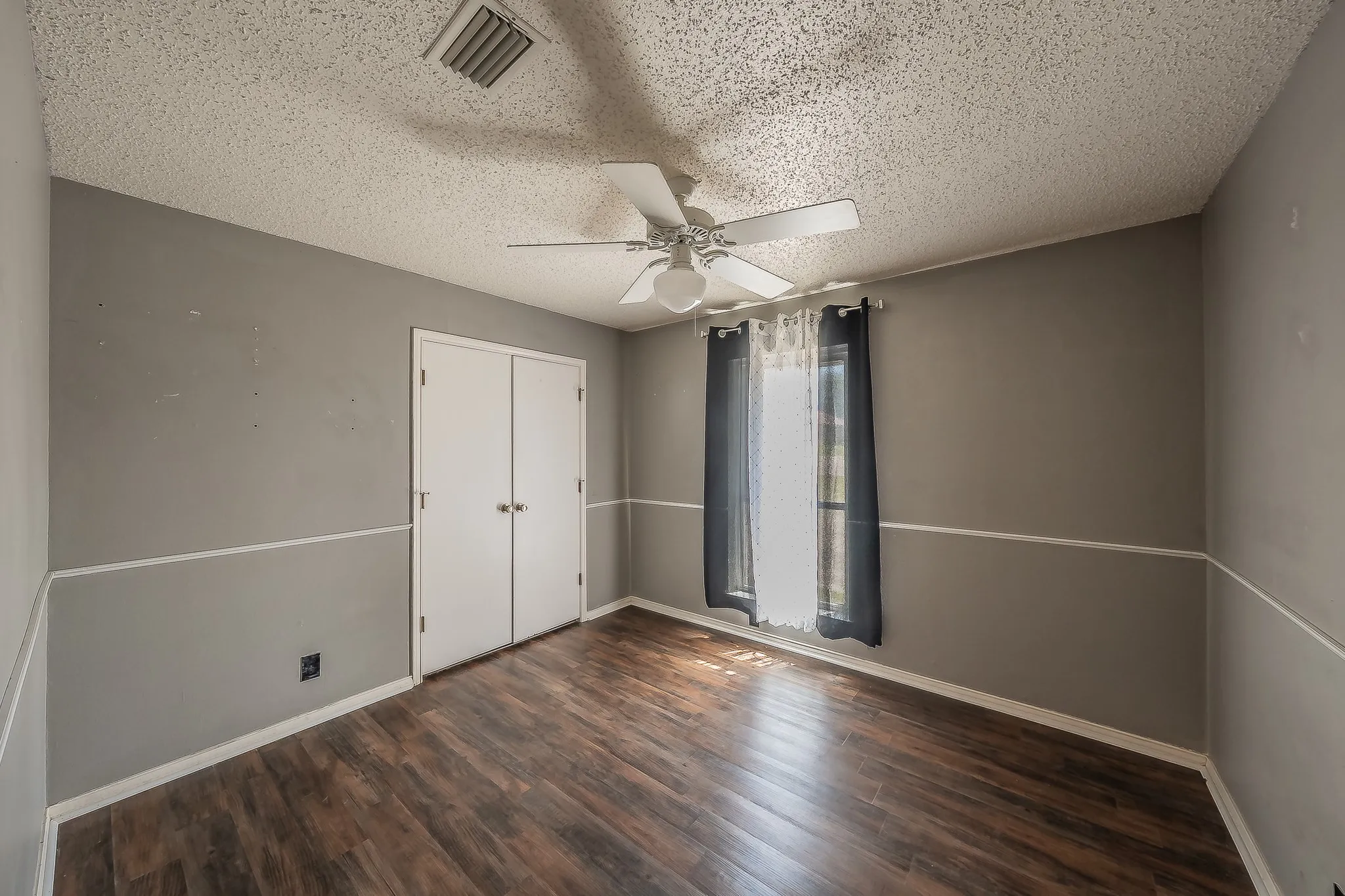 Room featuring wood-finish flooring, two-tone painted walls with chair rail molding, and a ceiling fan with integrated lighting