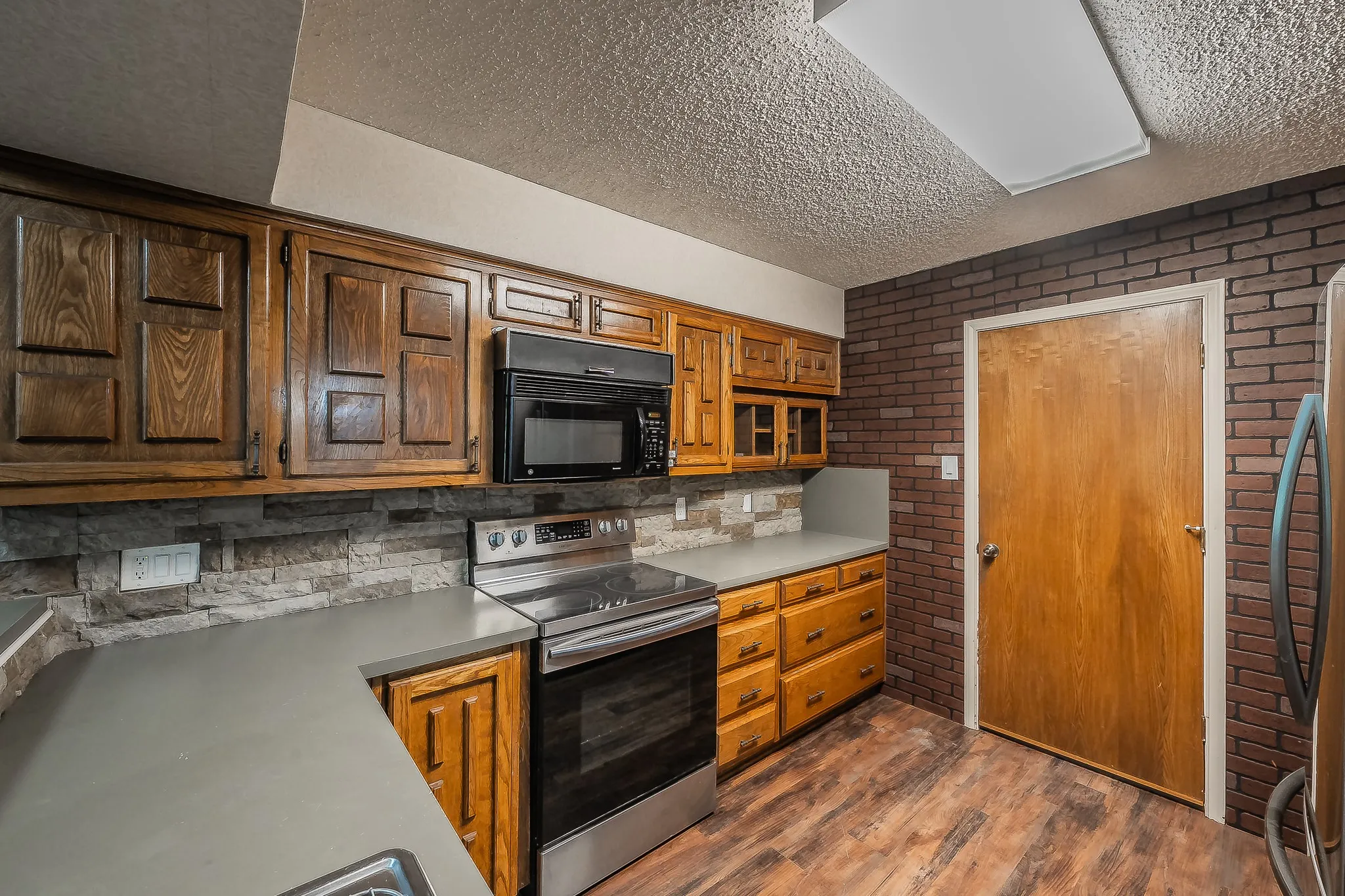 Kitchen featuring wood cabinetry, stone-look backsplash, and grey countertops