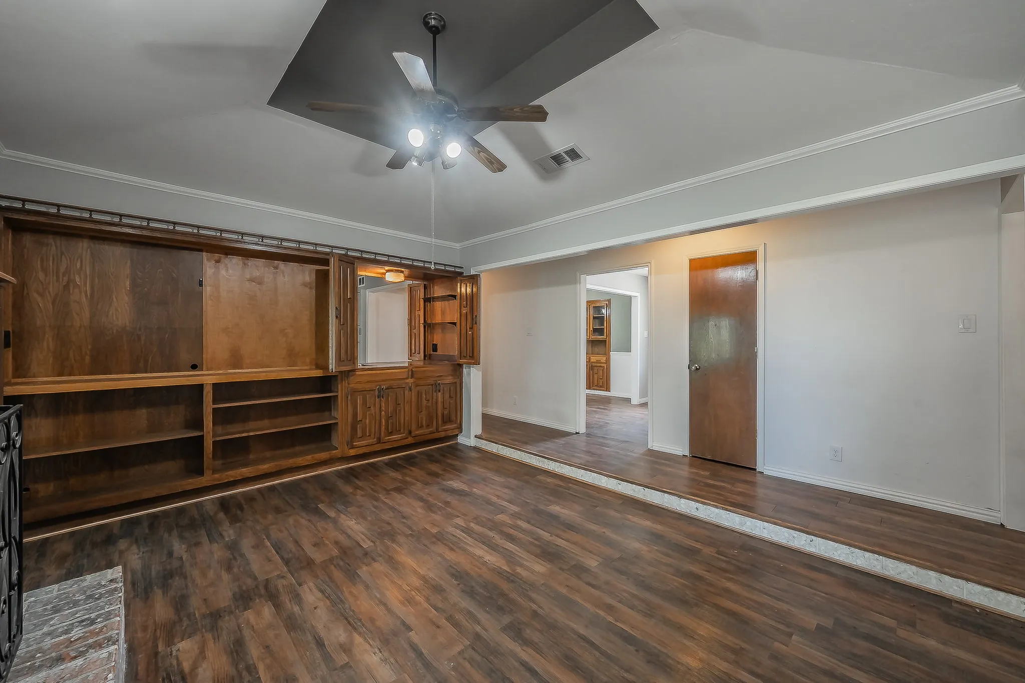 Spacious living area featuring wood-finish flooring, a built-in wood entertainment center with cabinetry, and a ceiling fan with integrated lighting