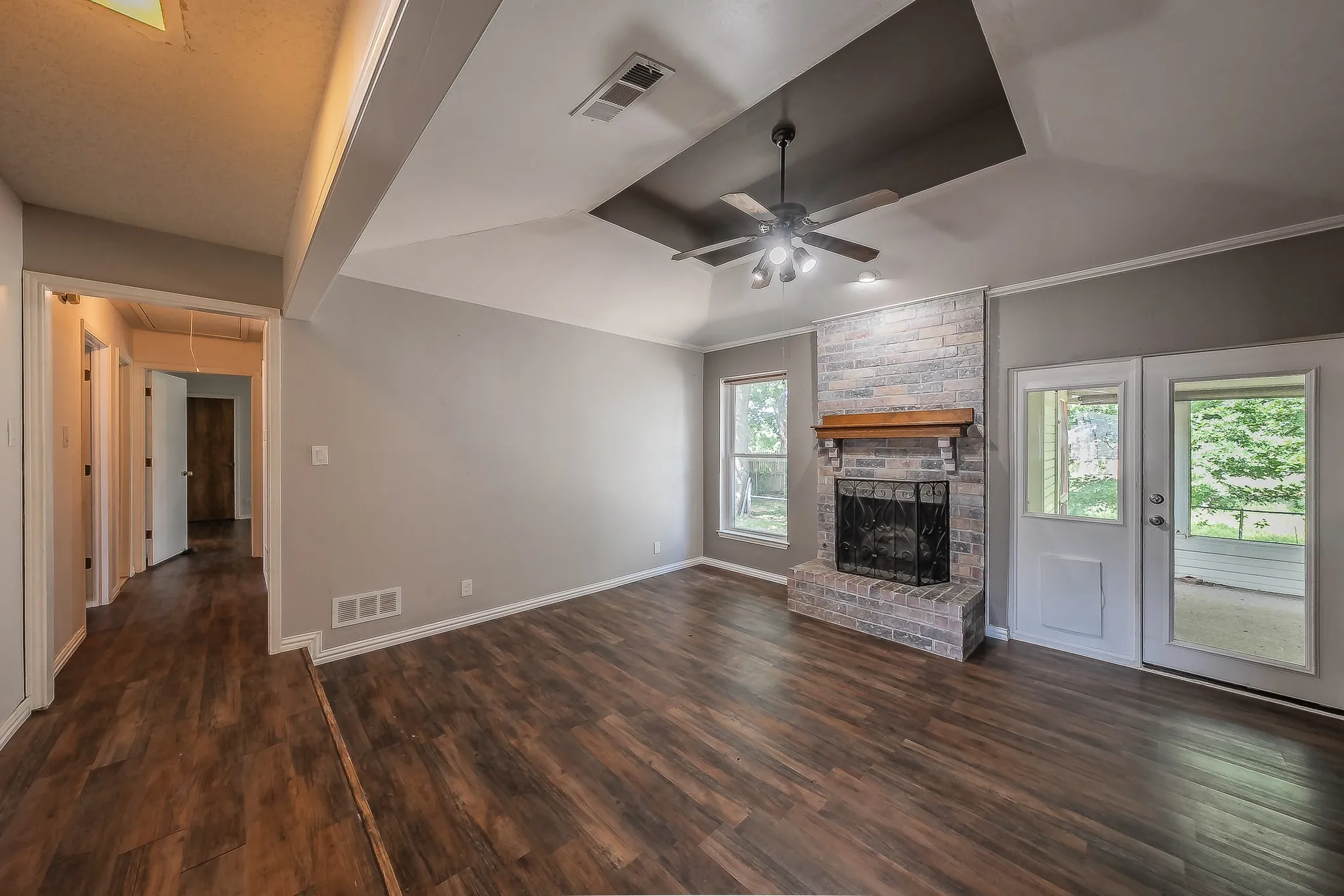Spacious living area featuring wood-finish flooring, a stone-faced fireplace with a wooden mantel, and a ceiling fan