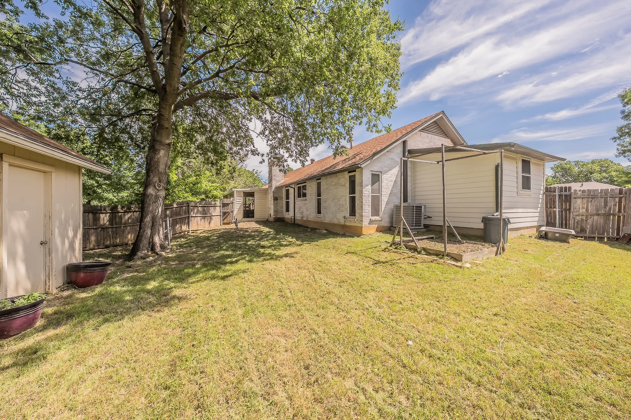 Expansive backyard featuring a mature shade tree, a separate storage shed, a wood fence perimeter, and a covered patio structure