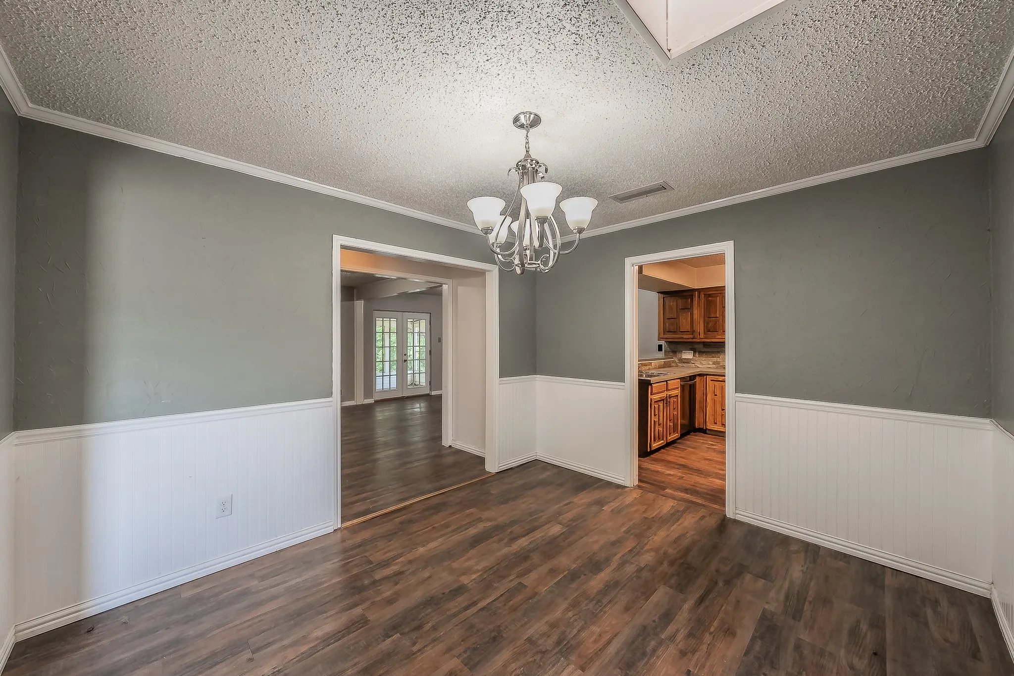 Dining area featuring wood-finish flooring, wainscoting, a ceiling-mounted chandelier, and crown molding