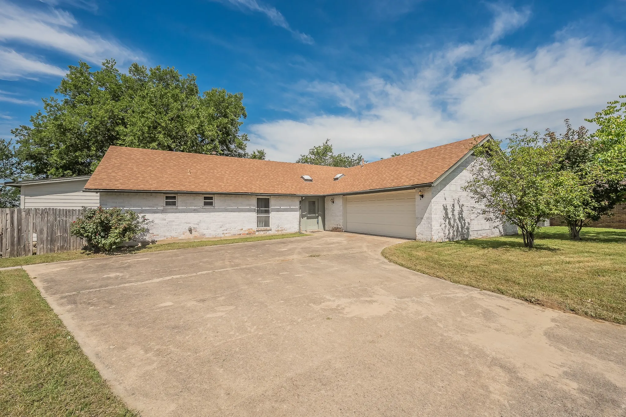 Ranch-style exterior with a brown shingle roof, white painted brick, and an attached two-car garage
