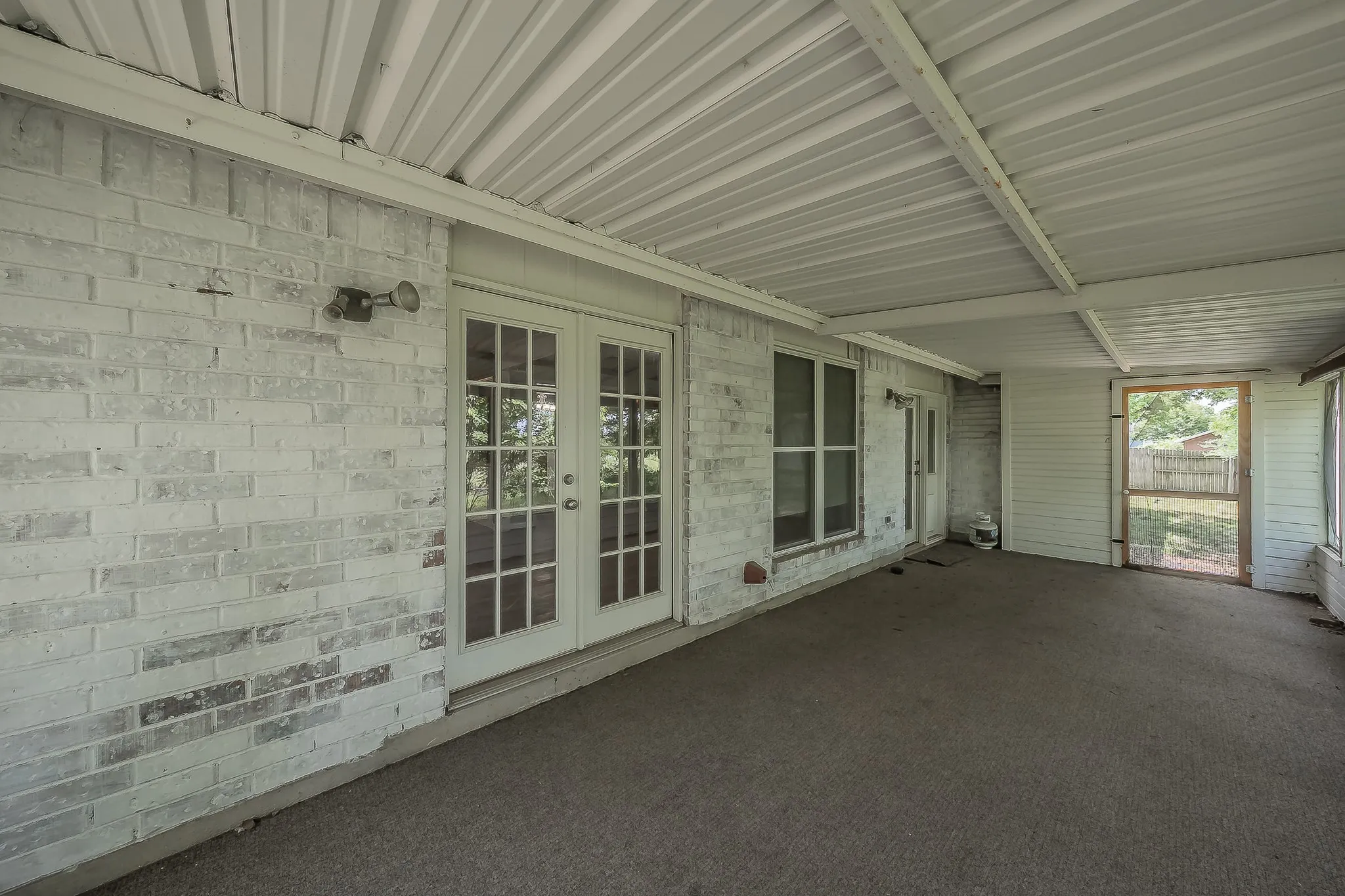 Covered patio featuring a white corrugated metal roof, painted brick exterior, and French doors with multiple lites
