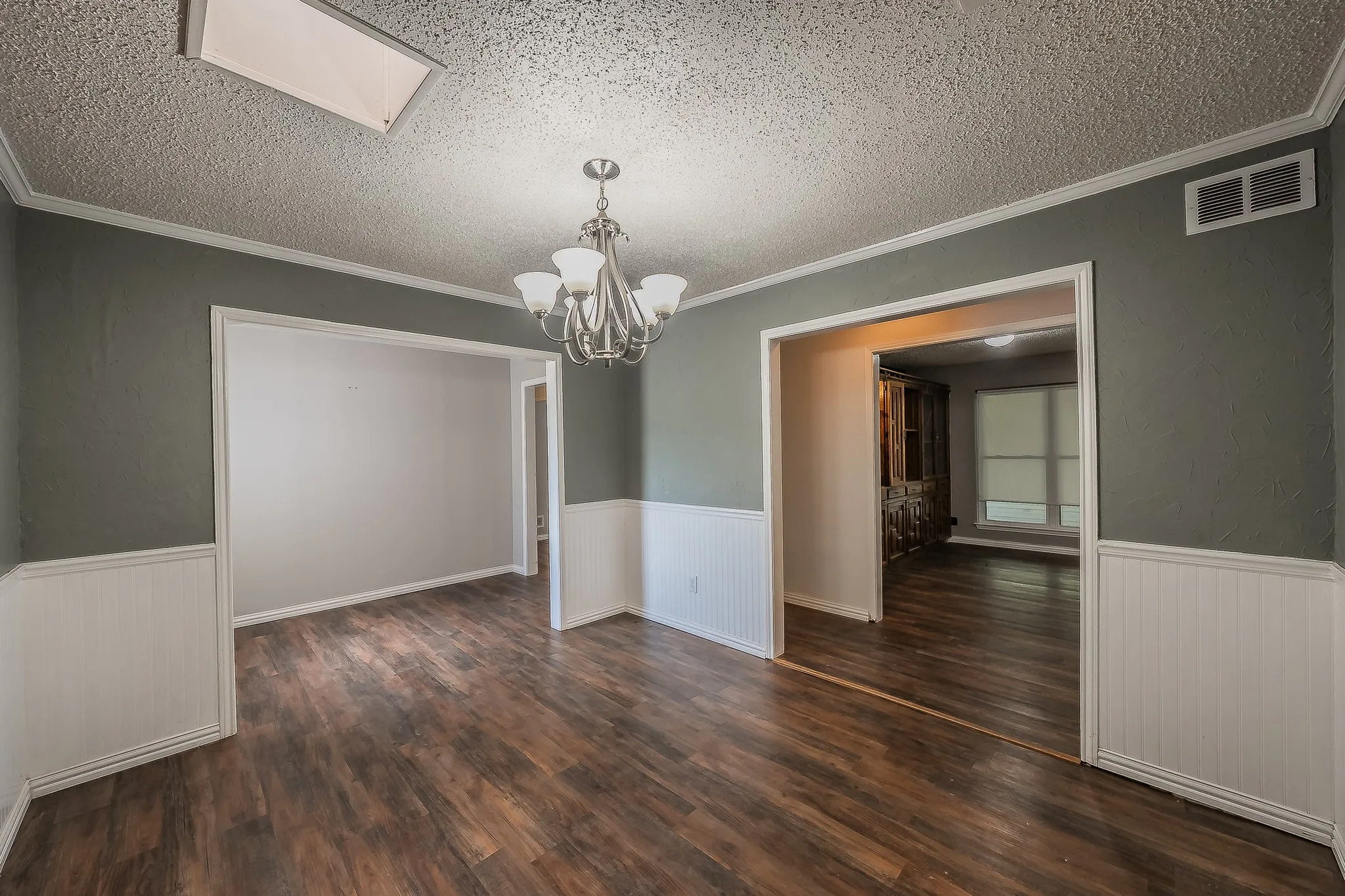 Spacious room featuring wood-finish flooring, white wainscoting, and a decorative chandelier