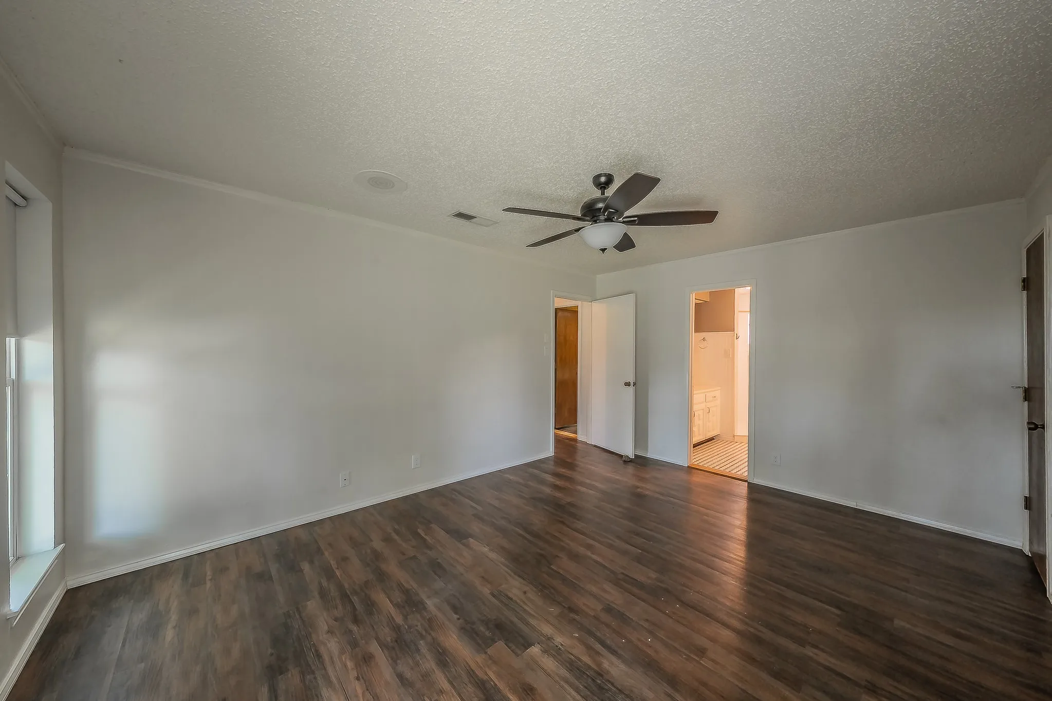 Spacious interior room featuring wood-finish flooring, white walls, and a ceiling fan with integrated lighting