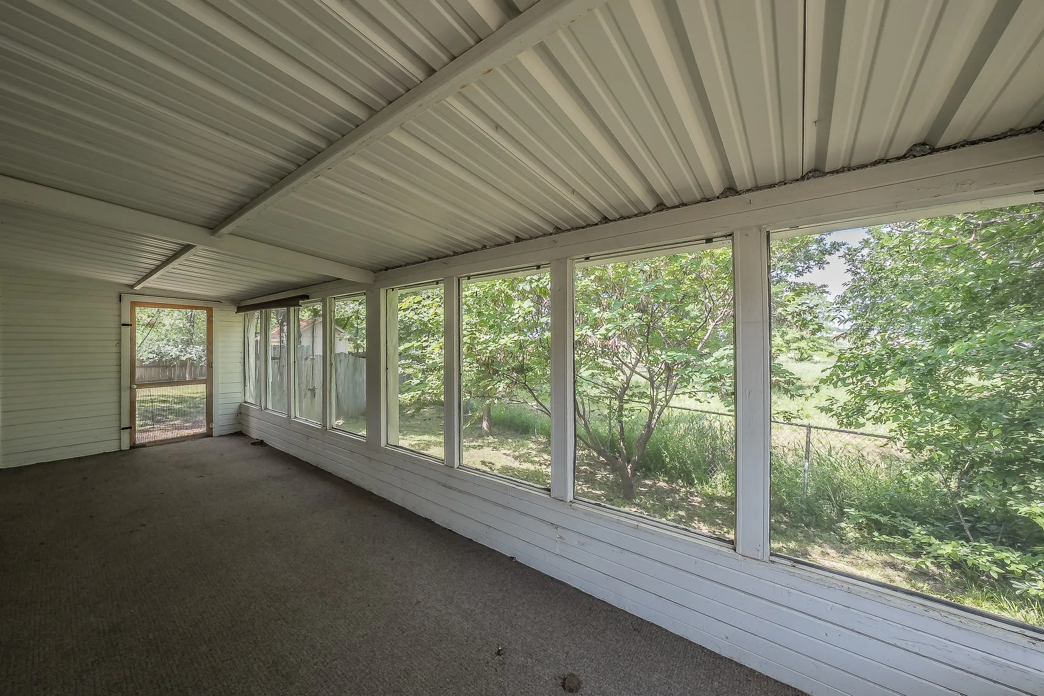 Screened-in porch featuring a corrugated metal ceiling, carpeted flooring, and a wall of windows overlooking a green landscape