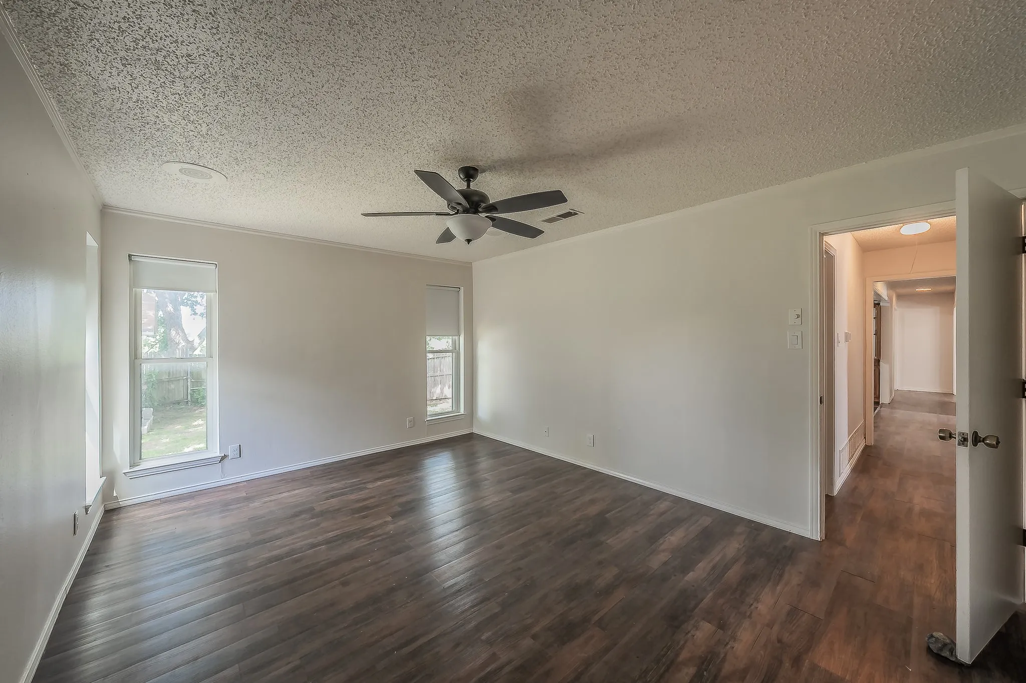 Spacious room with dark wood-finish flooring, white walls, and a textured ceiling