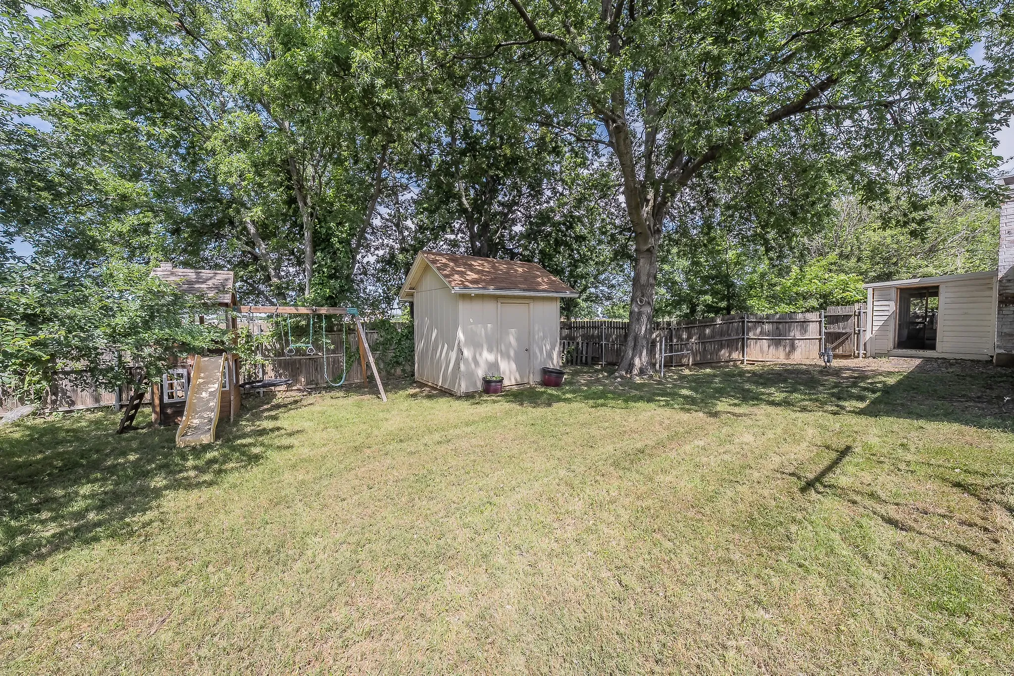 Expansive backyard featuring a privacy fence, mature trees, and two storage sheds
