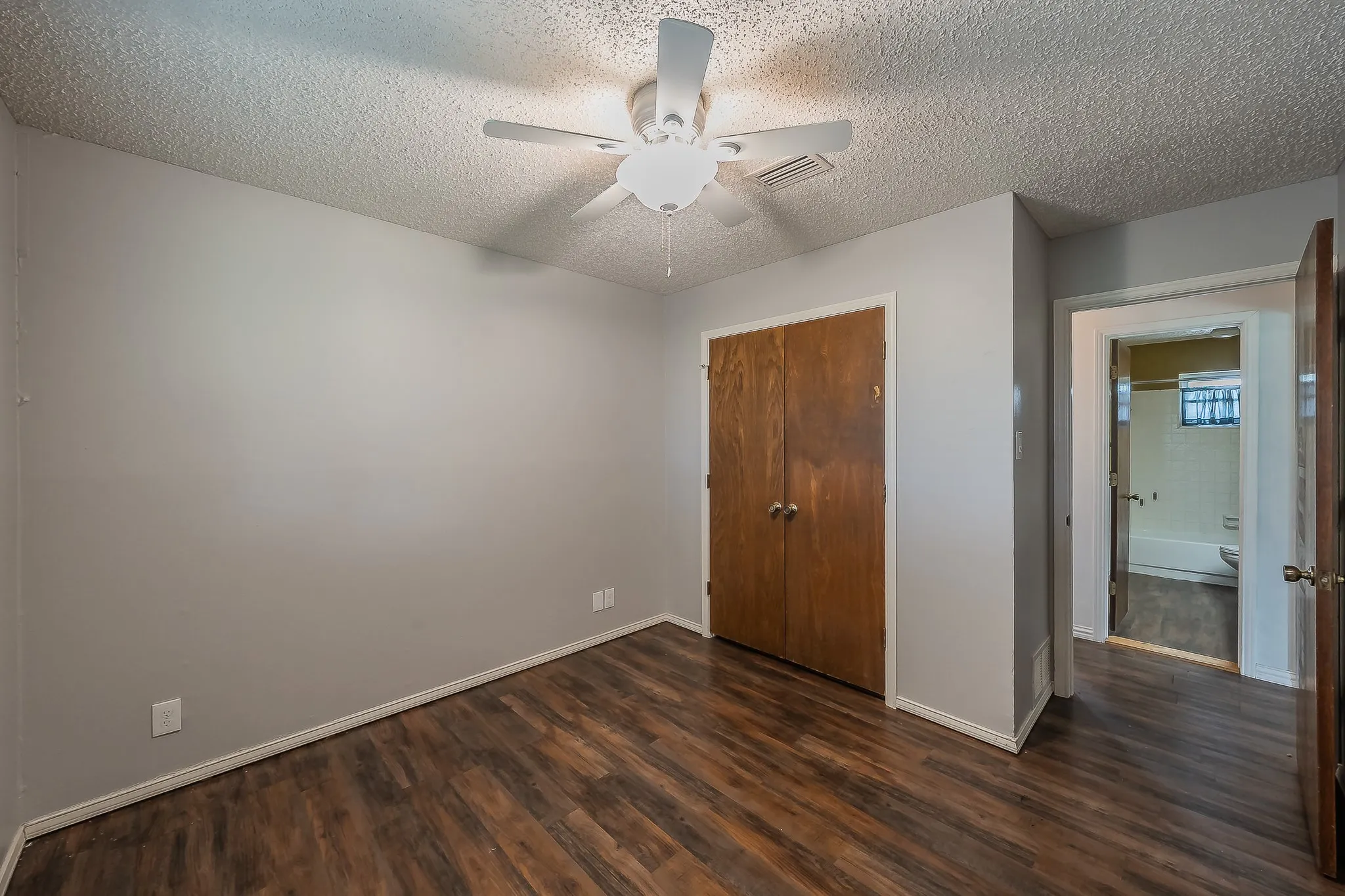 Spacious room featuring wood-finish flooring, light grey walls, and a ceiling fan with integrated lighting
