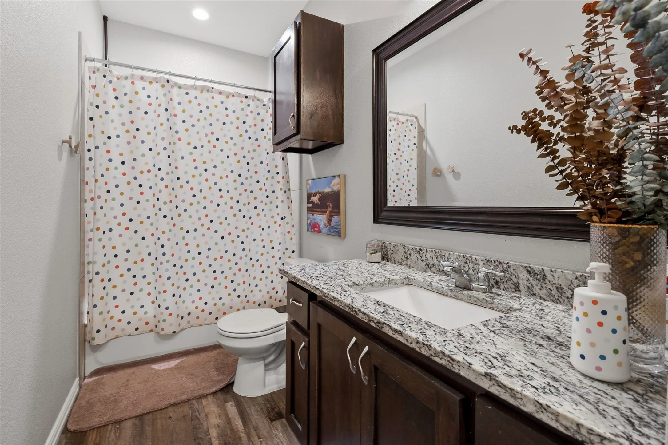 Bathroom featuring a white porcelain toilet, wood-finish flooring, a vanity with a white countertop, an undermount sink, and a framed mirror