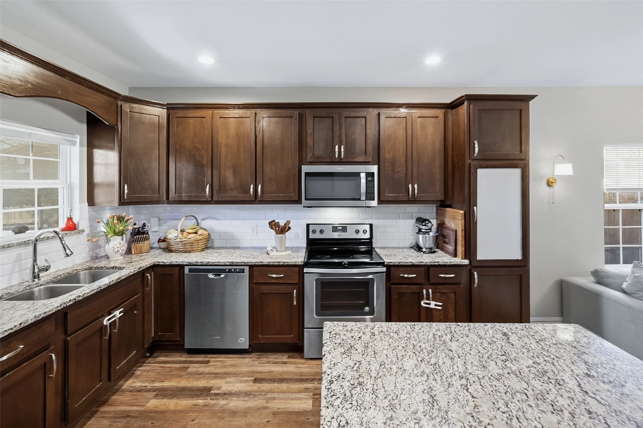 Kitchen featuring wood-finish cabinetry, stainless steel appliances, a double basin sink, light-toned countertops, and wood-finish flooring