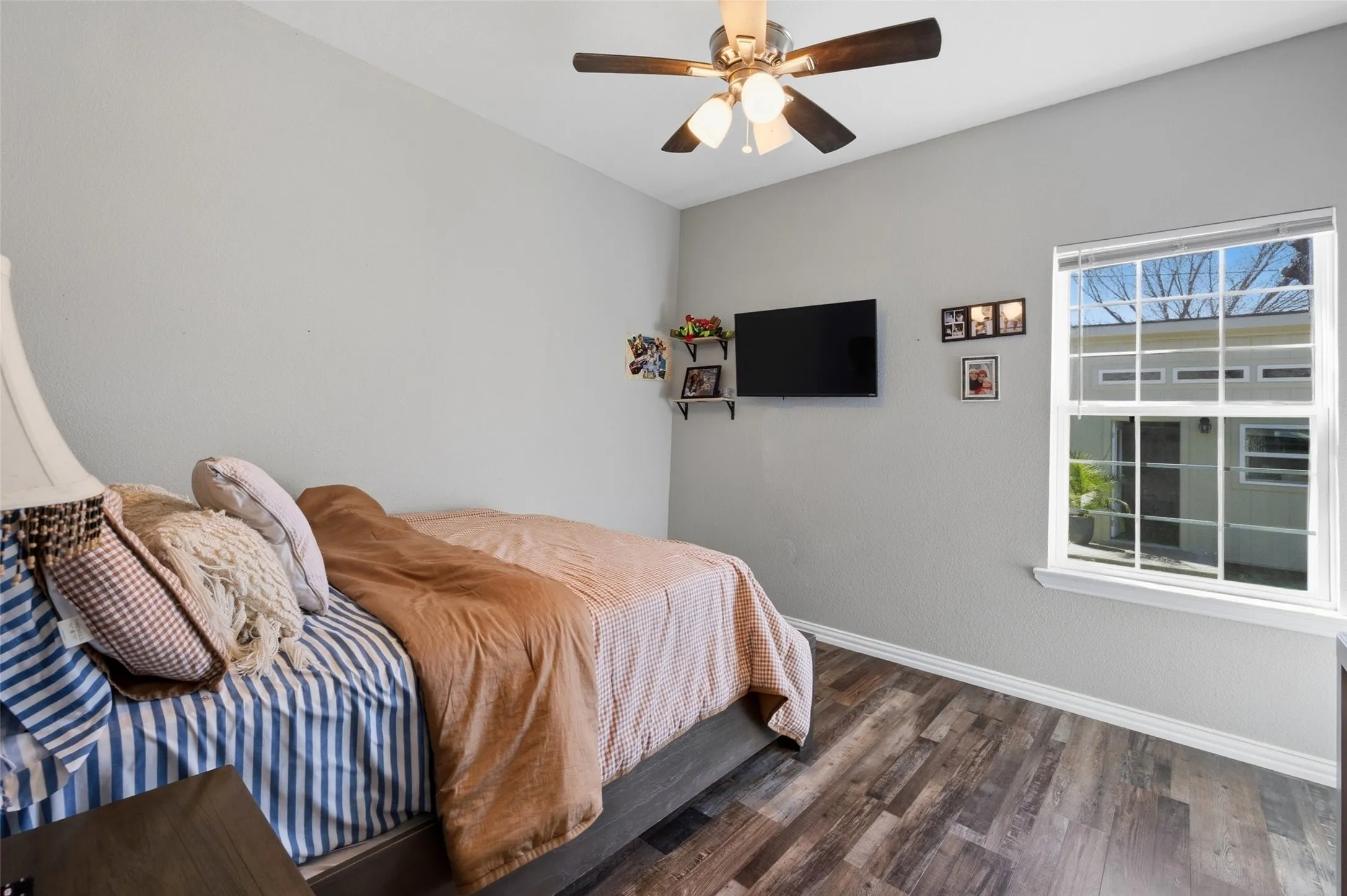 Room featuring wood-finish flooring, a ceiling fan with integrated lighting, and a single-pane window with white trim
