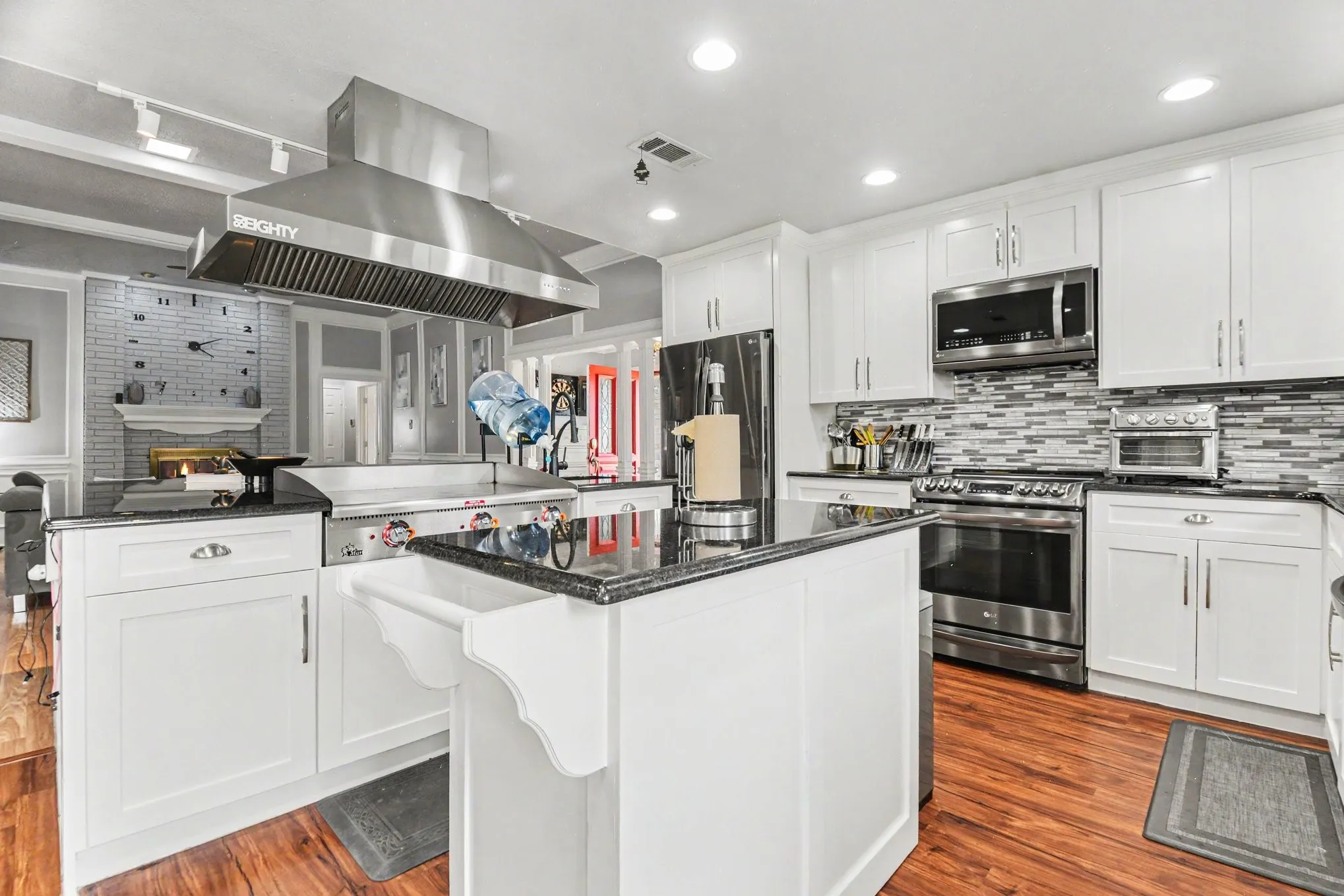Kitchen featuring white cabinetry, dark countertops, a stainless steel range hood, a tiled backsplash, and wood-finish flooring