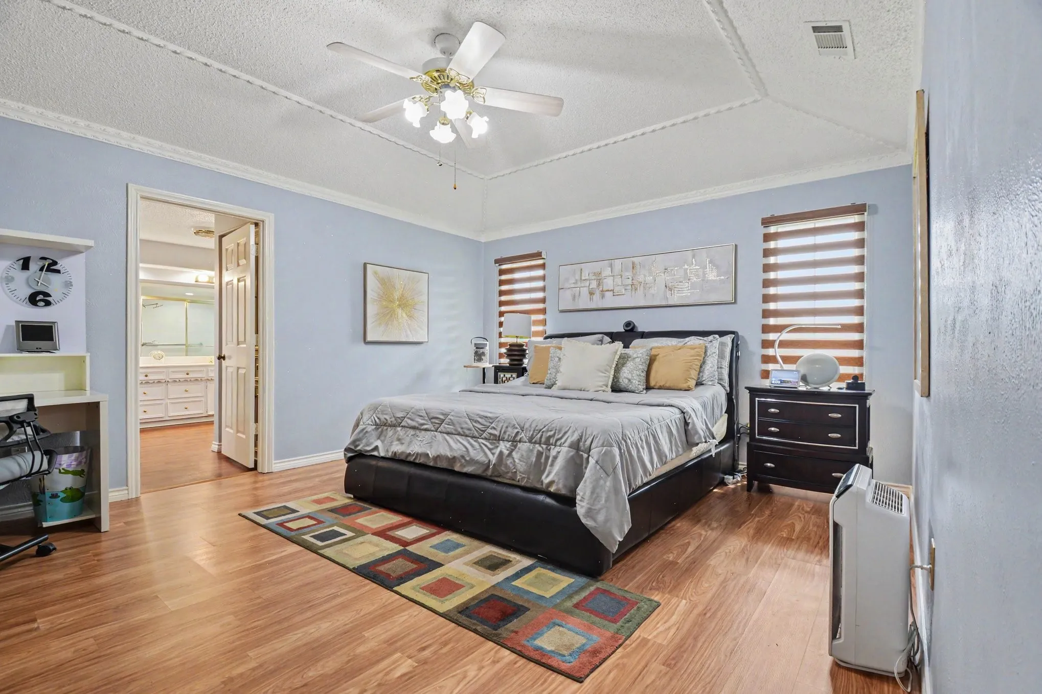 Spacious bedroom featuring wood-finish flooring and a tray ceiling with a fan light fixture