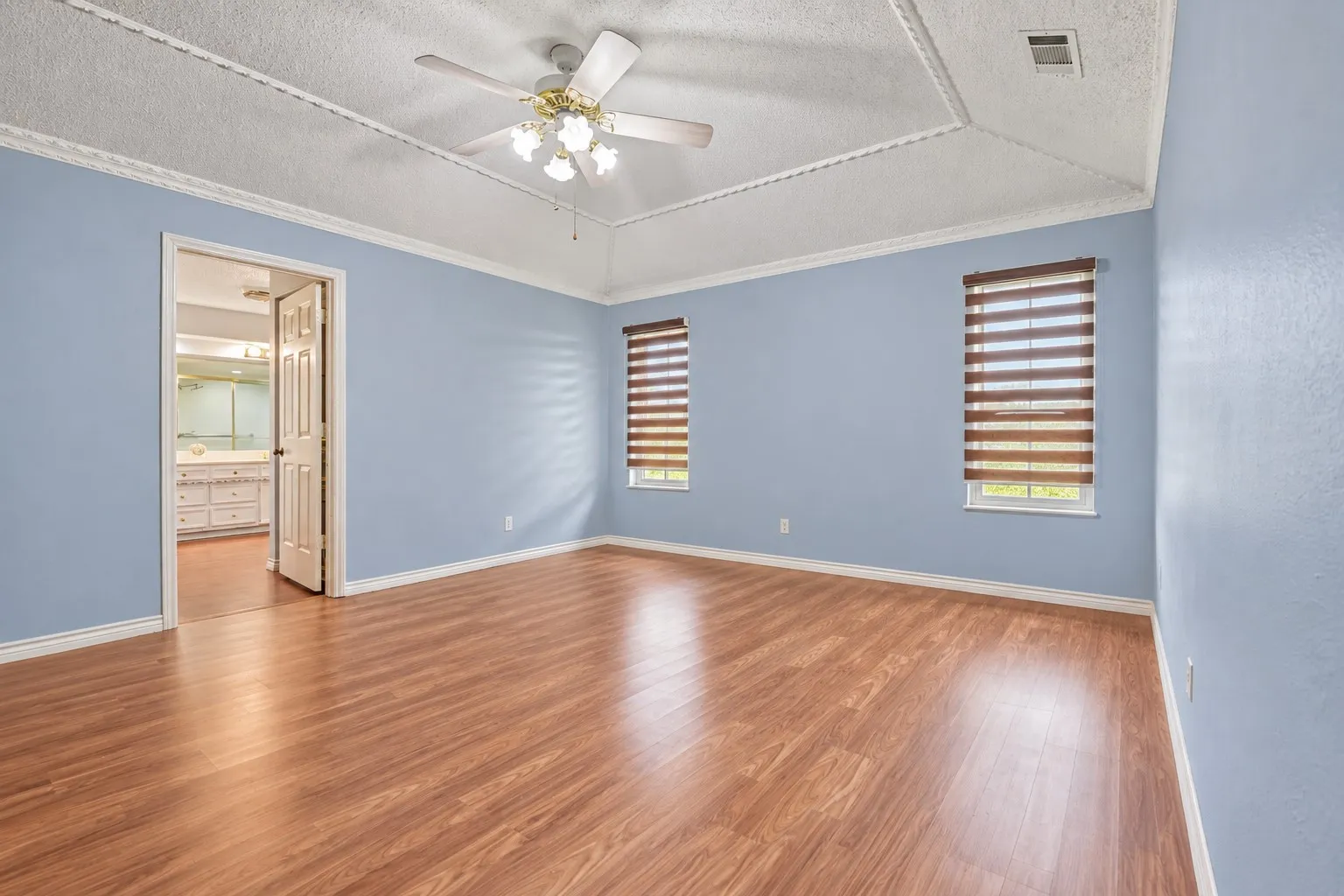 Master bedroom Wood-finish flooring, tray ceiling, crown molding, ceiling fan, and window blinds