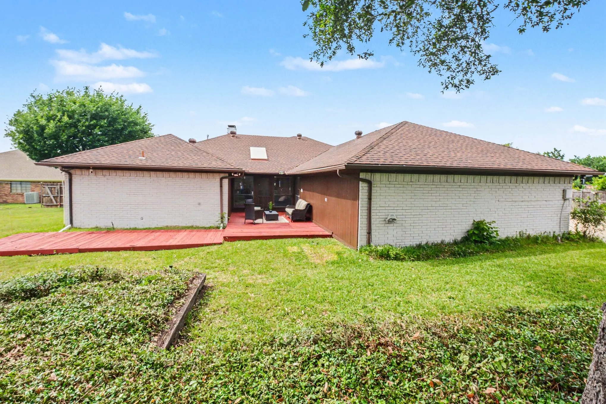 Expansive backyard featuring a red wood deck, a manicured lawn, and a light brick exterior