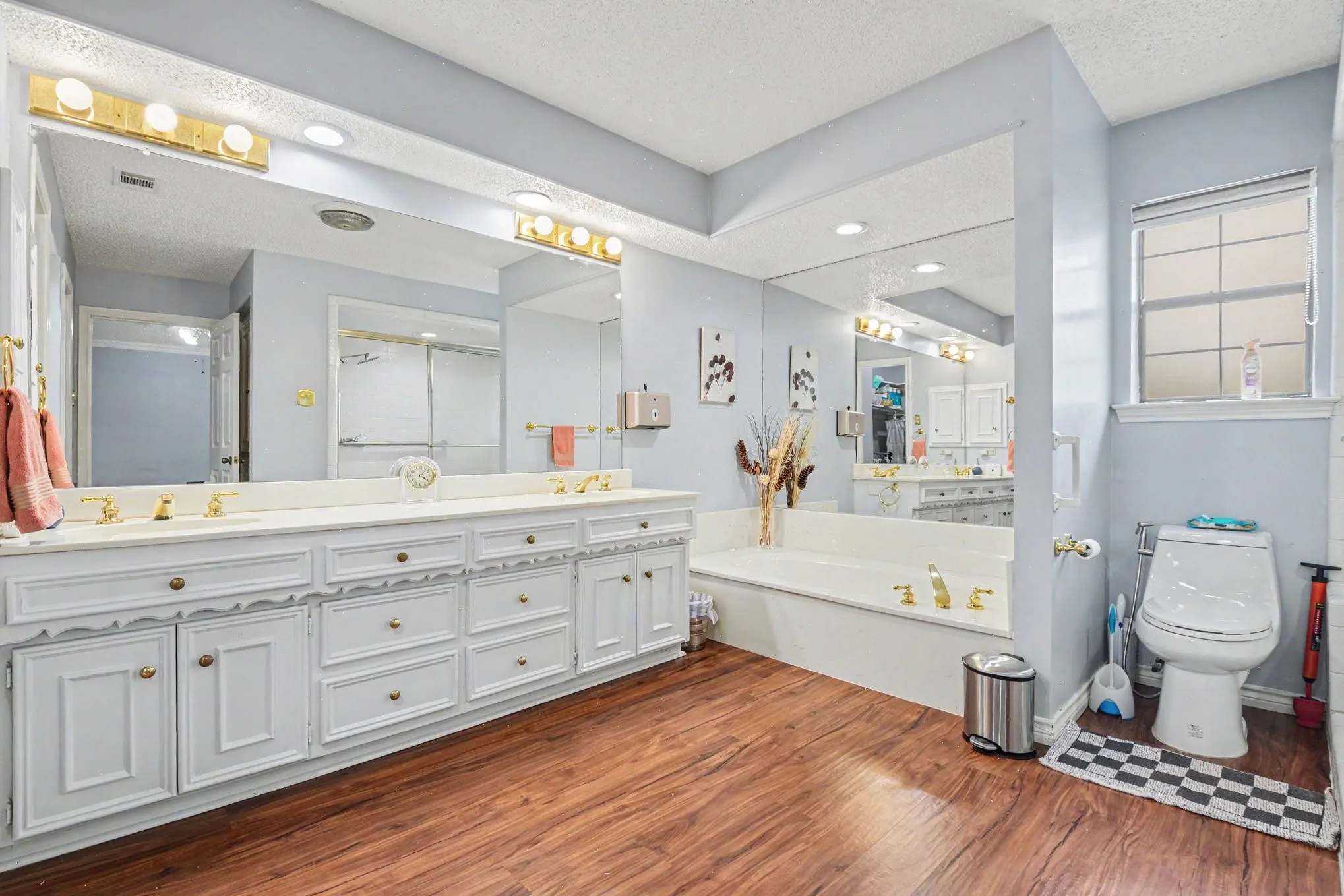 Double vanity featuring white cabinetry, gold-tone hardware, and a single-light window