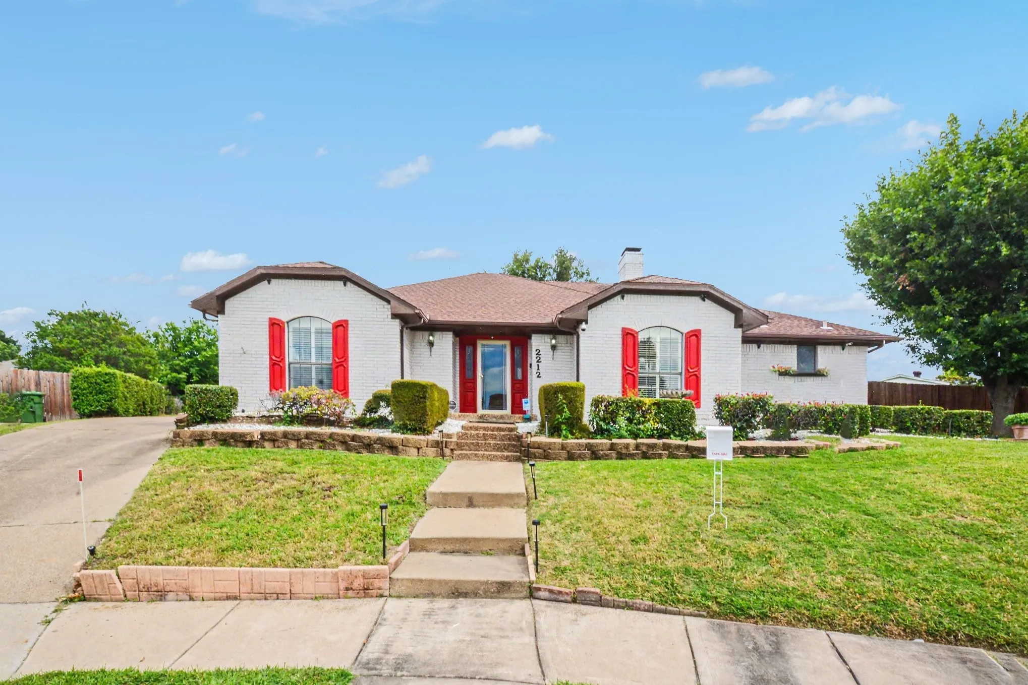 White brick exterior featuring a red front door and coordinating window shutters