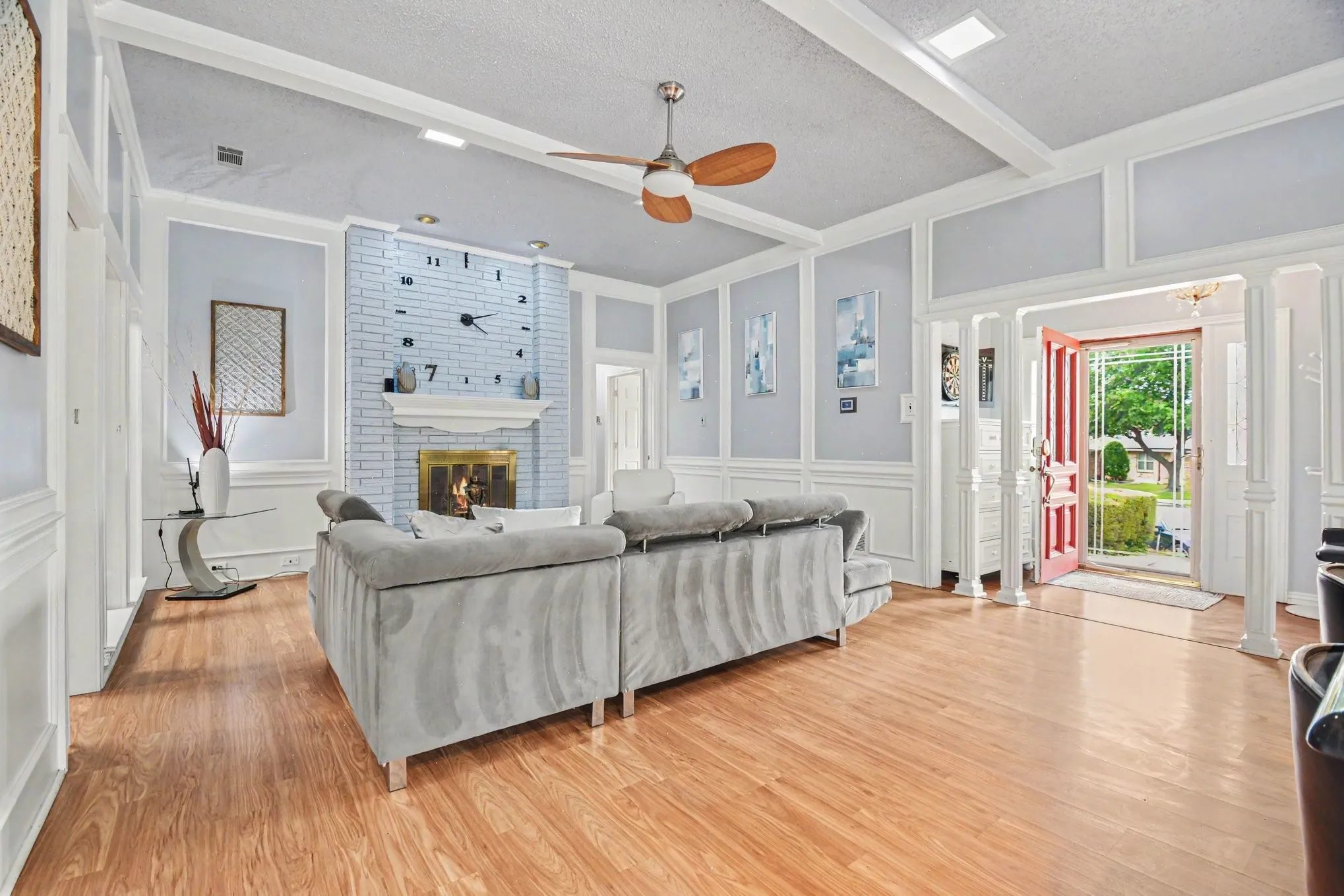Spacious living area featuring wood-finish flooring, a painted brick fireplace, and extensive wainscoting