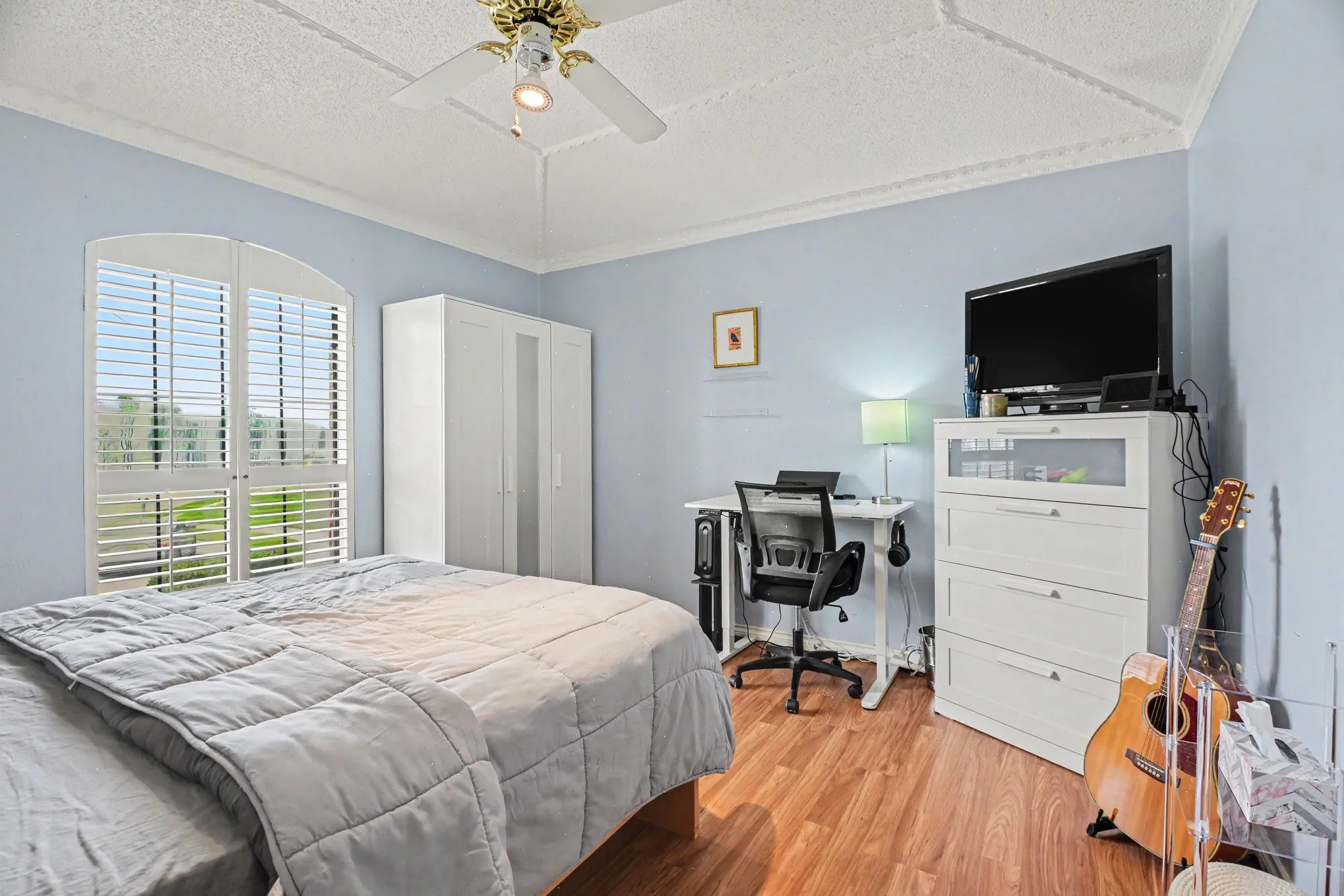 Arched window with plantation shutters, wood-finish flooring, ceiling fan, and decorative crown molding