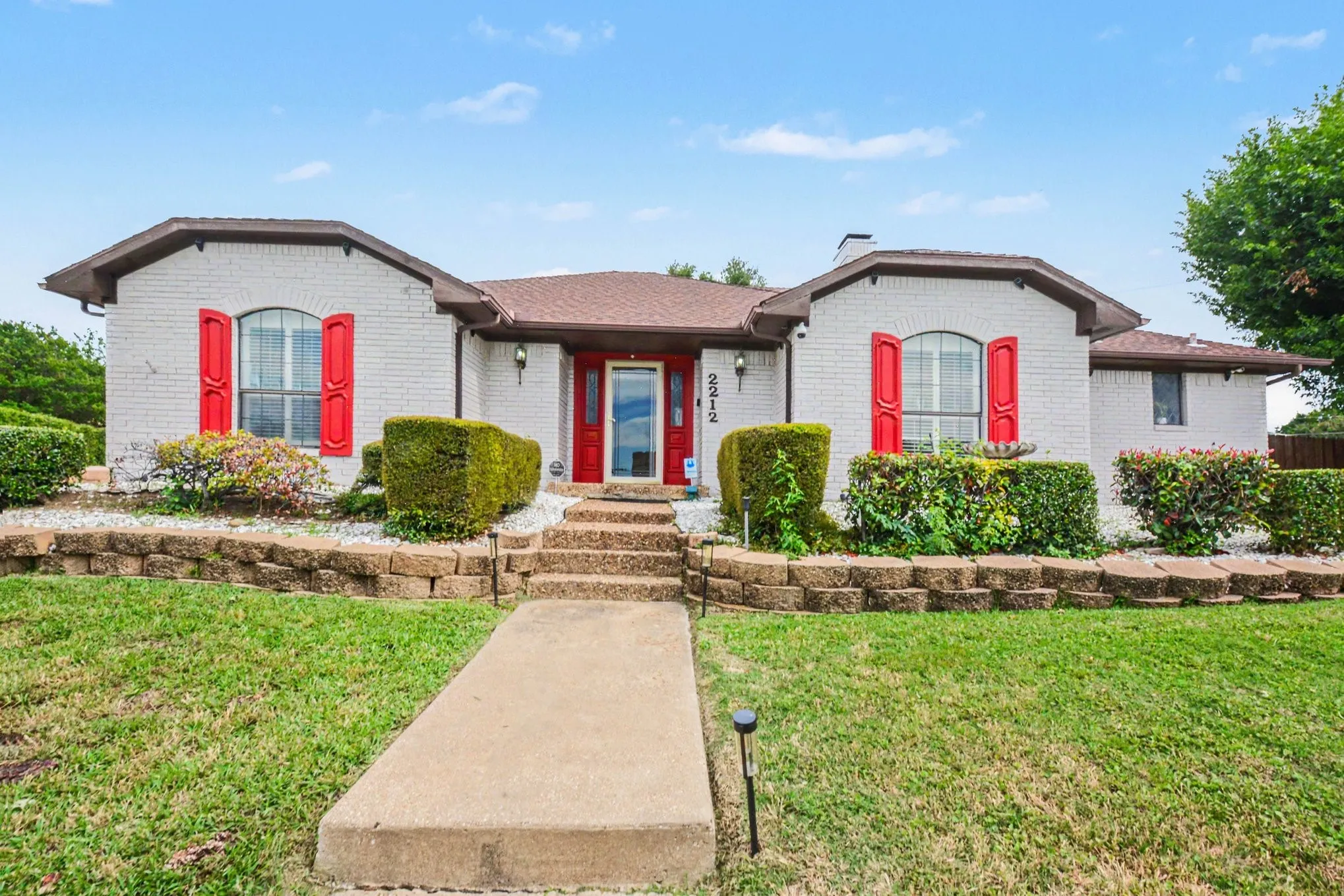White brick exterior with prominent red window shutters and a matching red front door