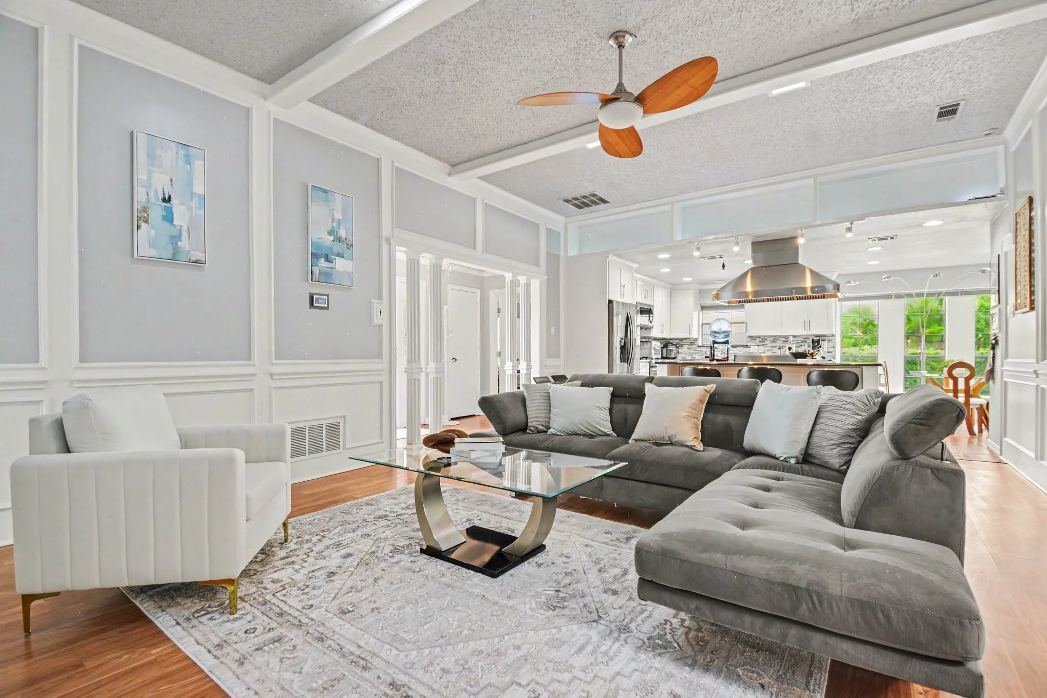 Open-concept living area featuring wood-finish flooring, white decorative wall paneling, and a white coffered ceiling