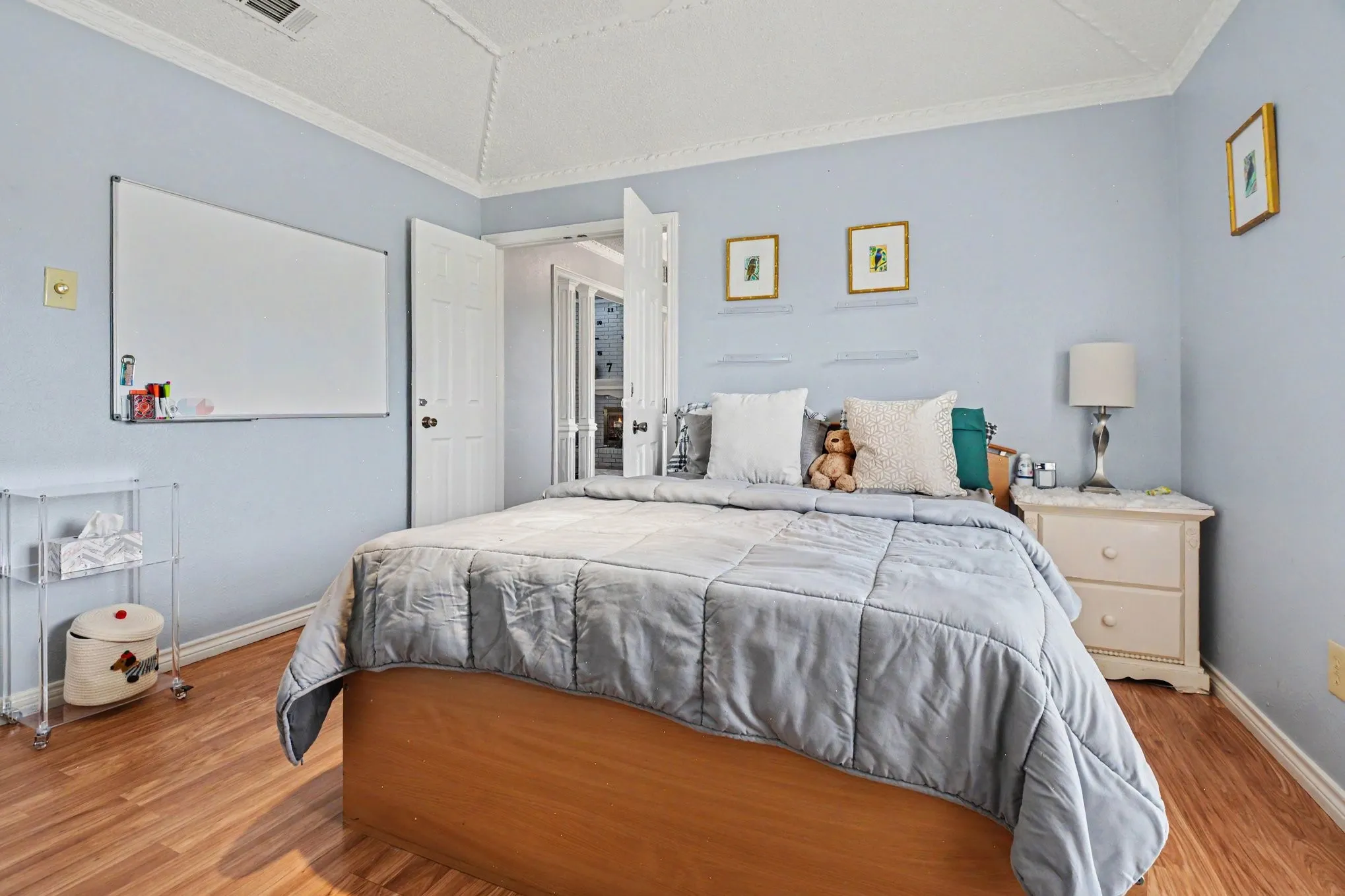 Light blue walls featuring wood-finish flooring, a tray ceiling with crown molding, a built-in closet with bi-fold doors, and a built-in nightstand with two drawers