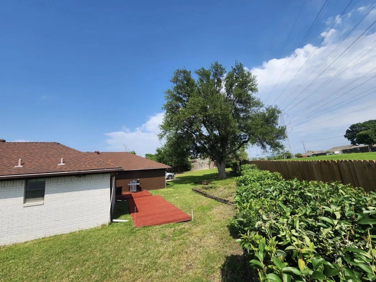 Expansive backyard featuring a large shade tree, wood privacy fence, and manicured shrubbery