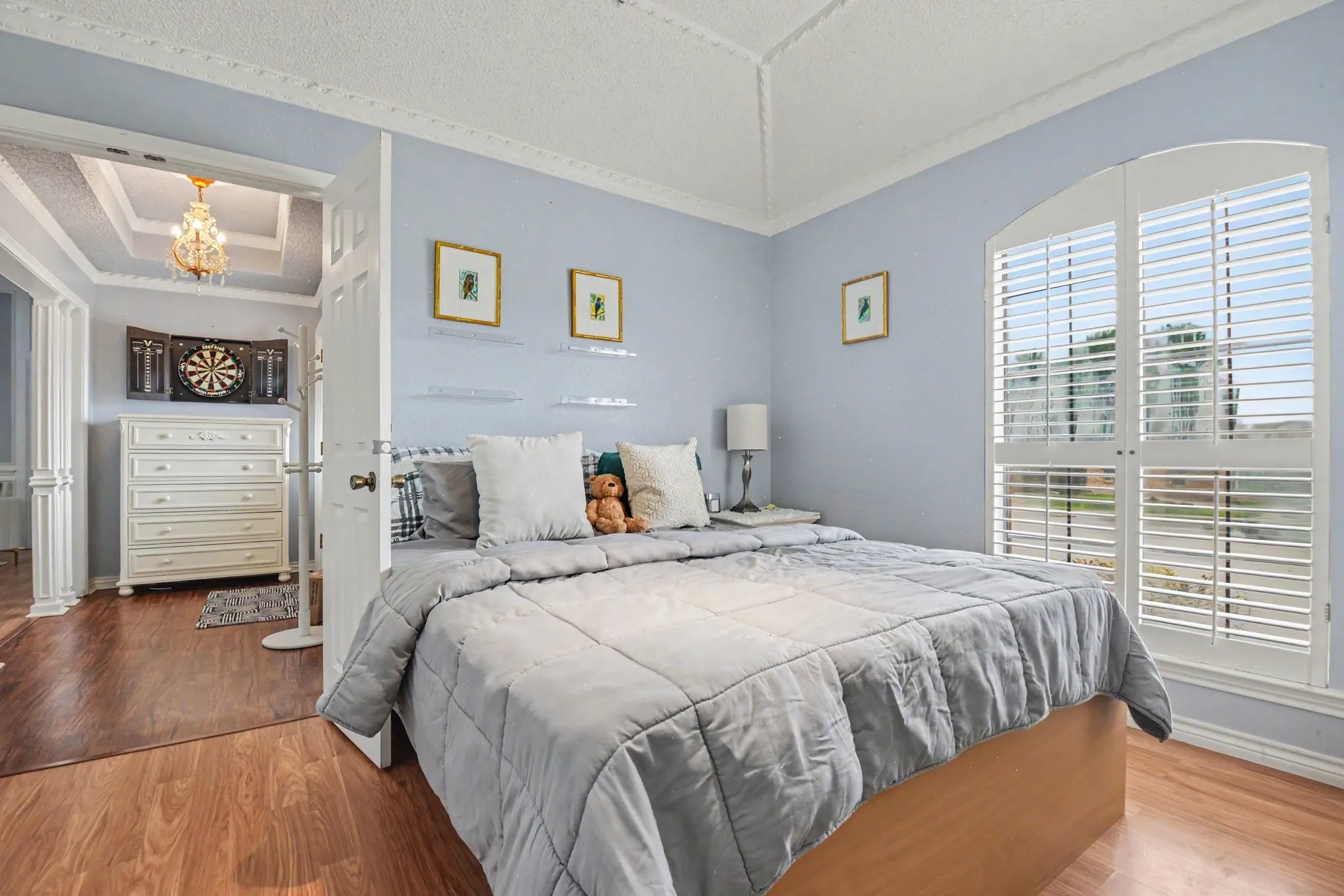 Room featuring wood-finish flooring, a vaulted ceiling with crown molding, and an arched window with white louvered shutters