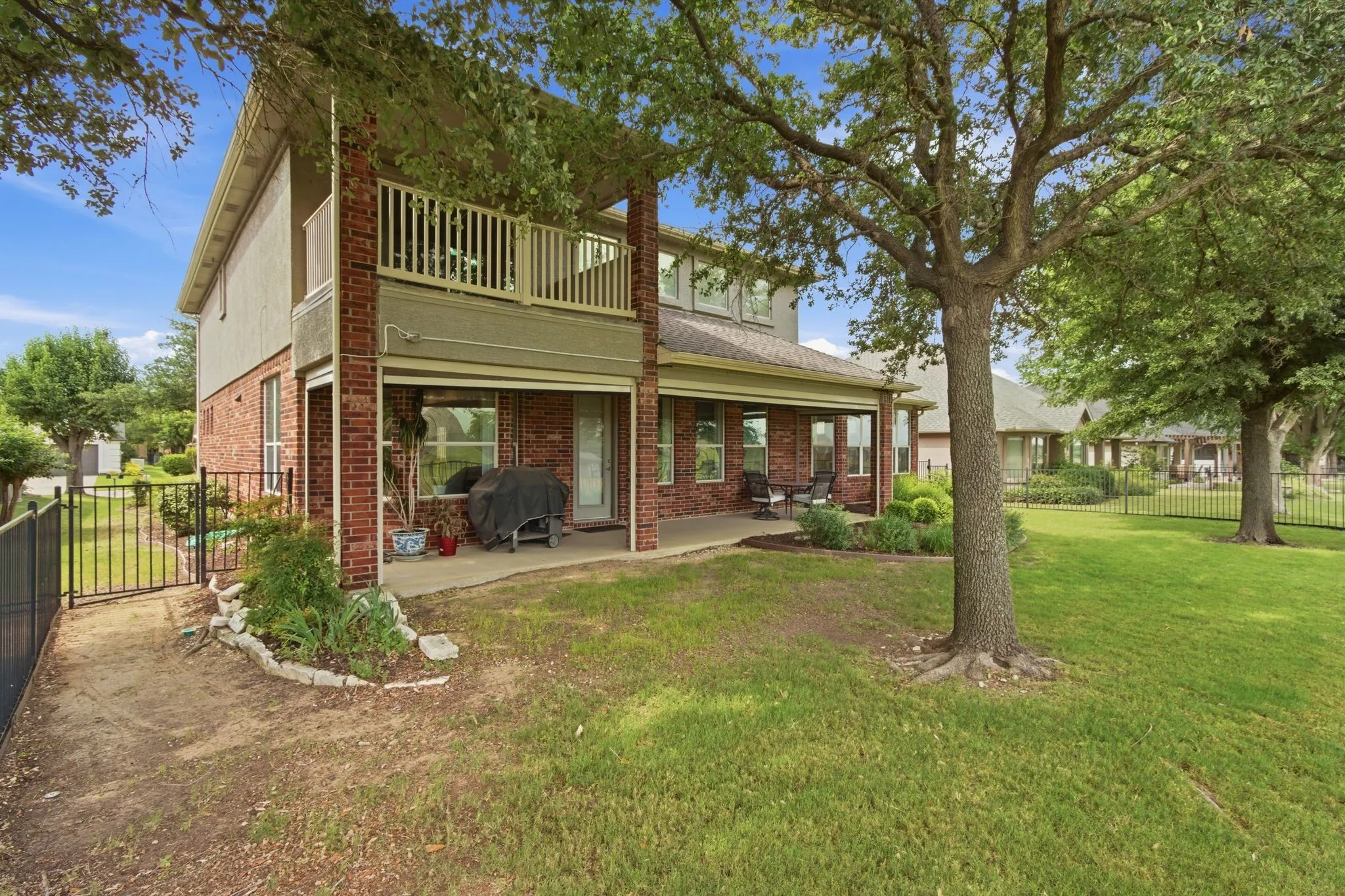 Spacious backyard featuring a manicured lawn, mature trees, and a black metal fence