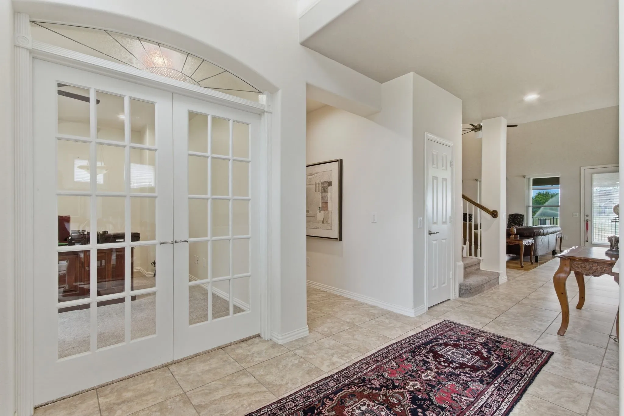 Entryway features tile flooring, white French doors with an arched transom leads into  the den/study.