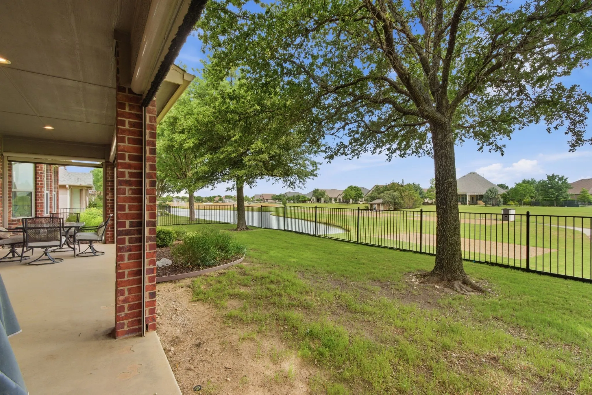 Patio with motorized screens and fenced yard overlooking an expansive green featuring a large pond and manicured lawn.