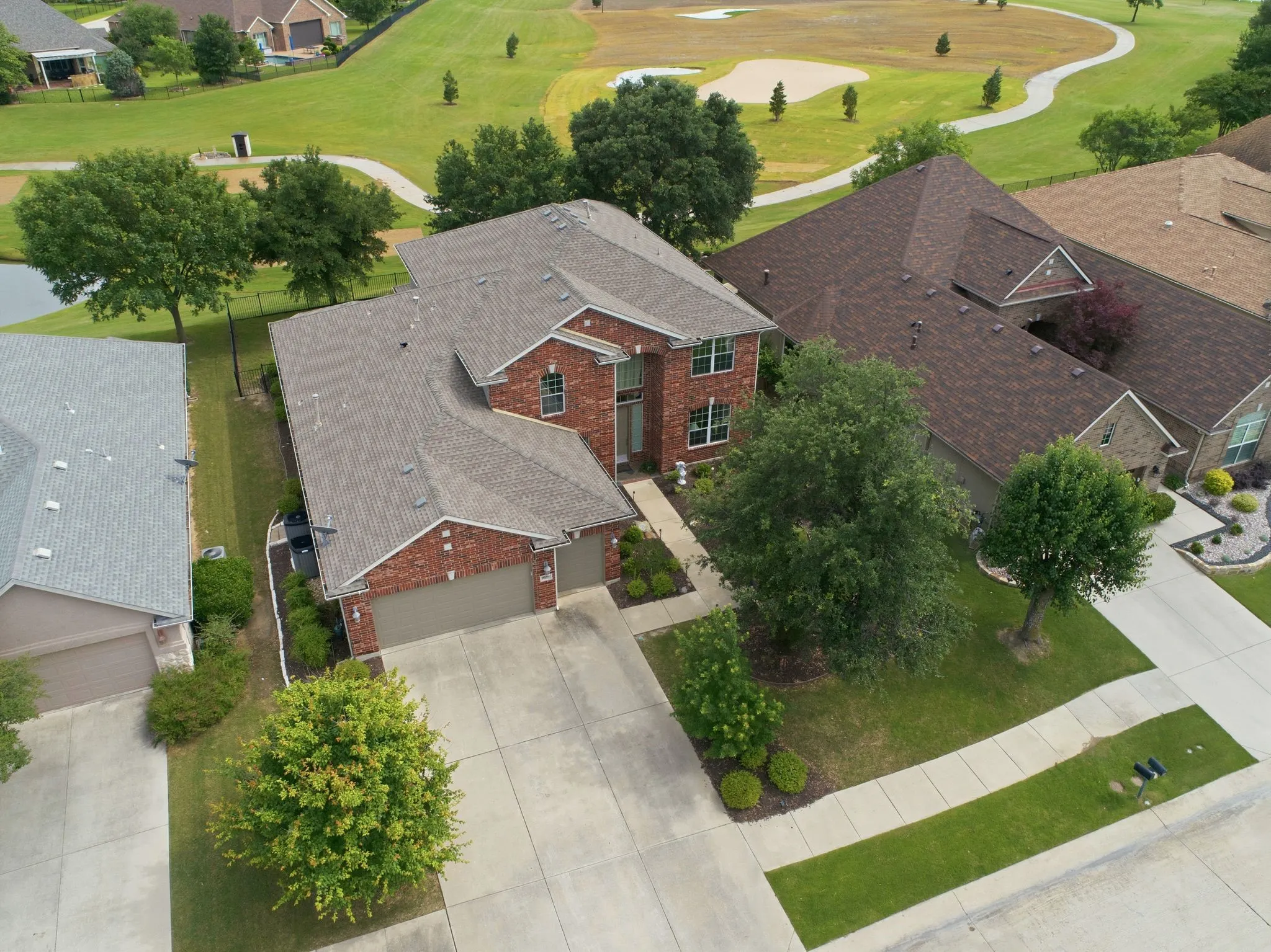 Aerial perspective of a residential neighborhood featuring a golf course with putting greens and sand traps, and a pond