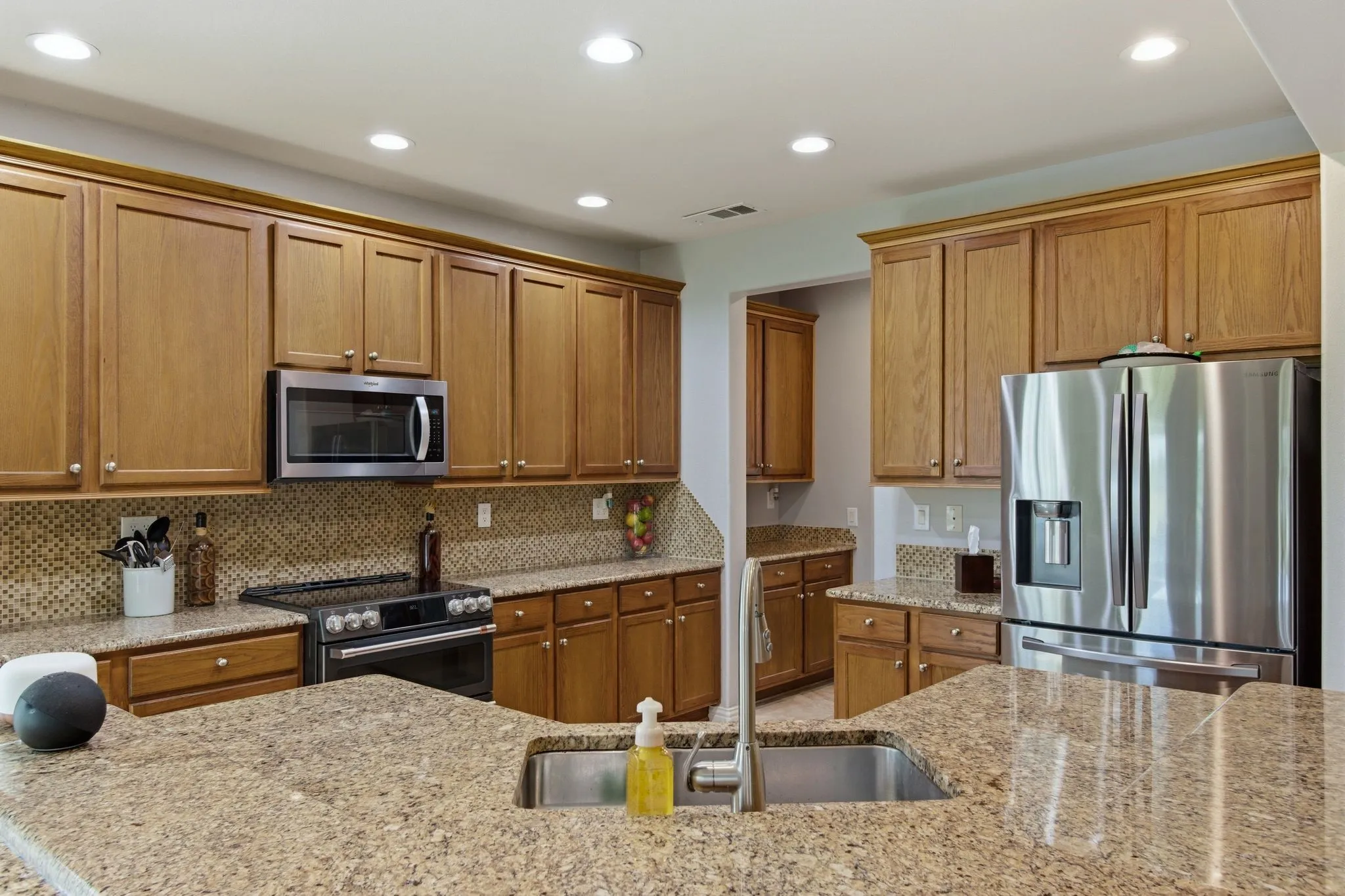 Spacious kitchen featuring granite countertops, wood cabinetry, stainless steel appliances, a tile backsplash, and recessed lighting