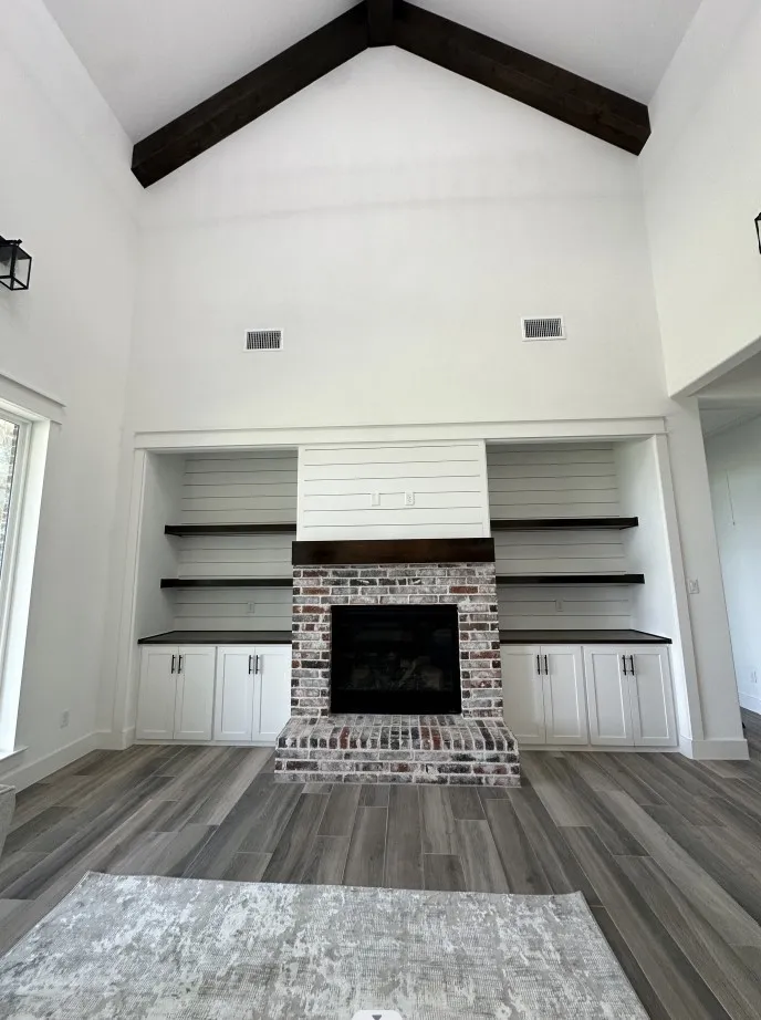 Unfurnished living room featuring high vaulted ceiling, wood finished floors, beam ceiling, and a brick fireplace
