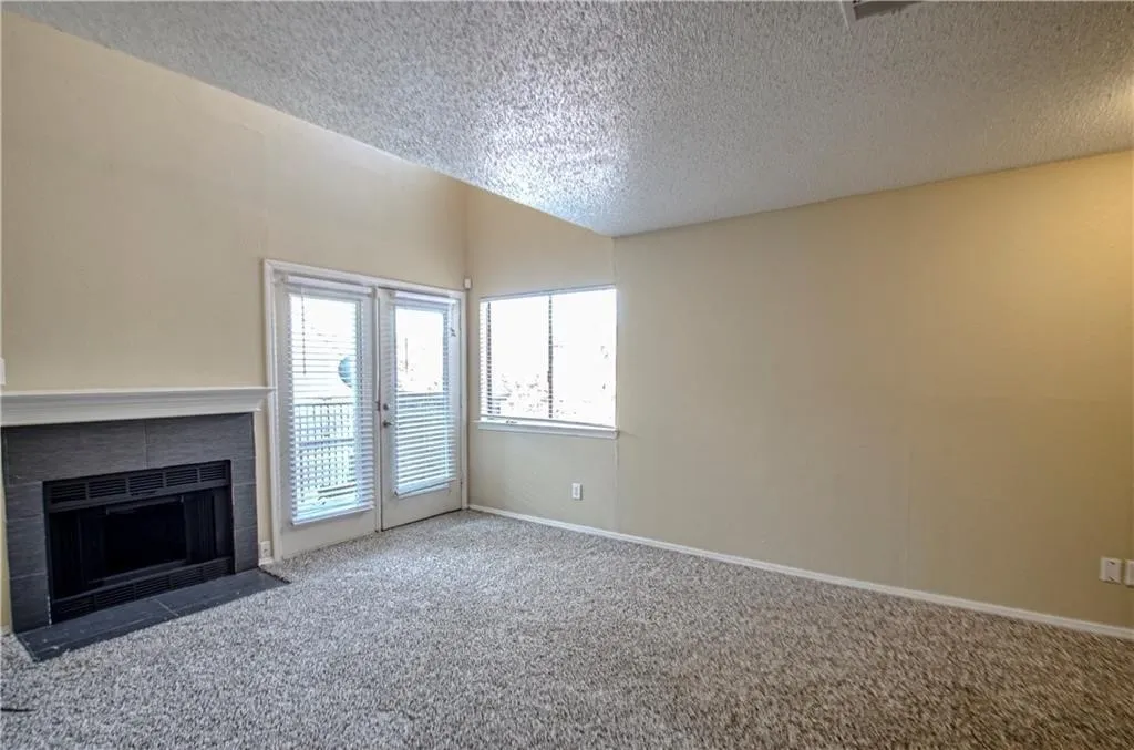 Living area featuring a textured ceiling, a fireplace with a dark tile surround and white mantel, light-colored walls, and gray carpet flooring