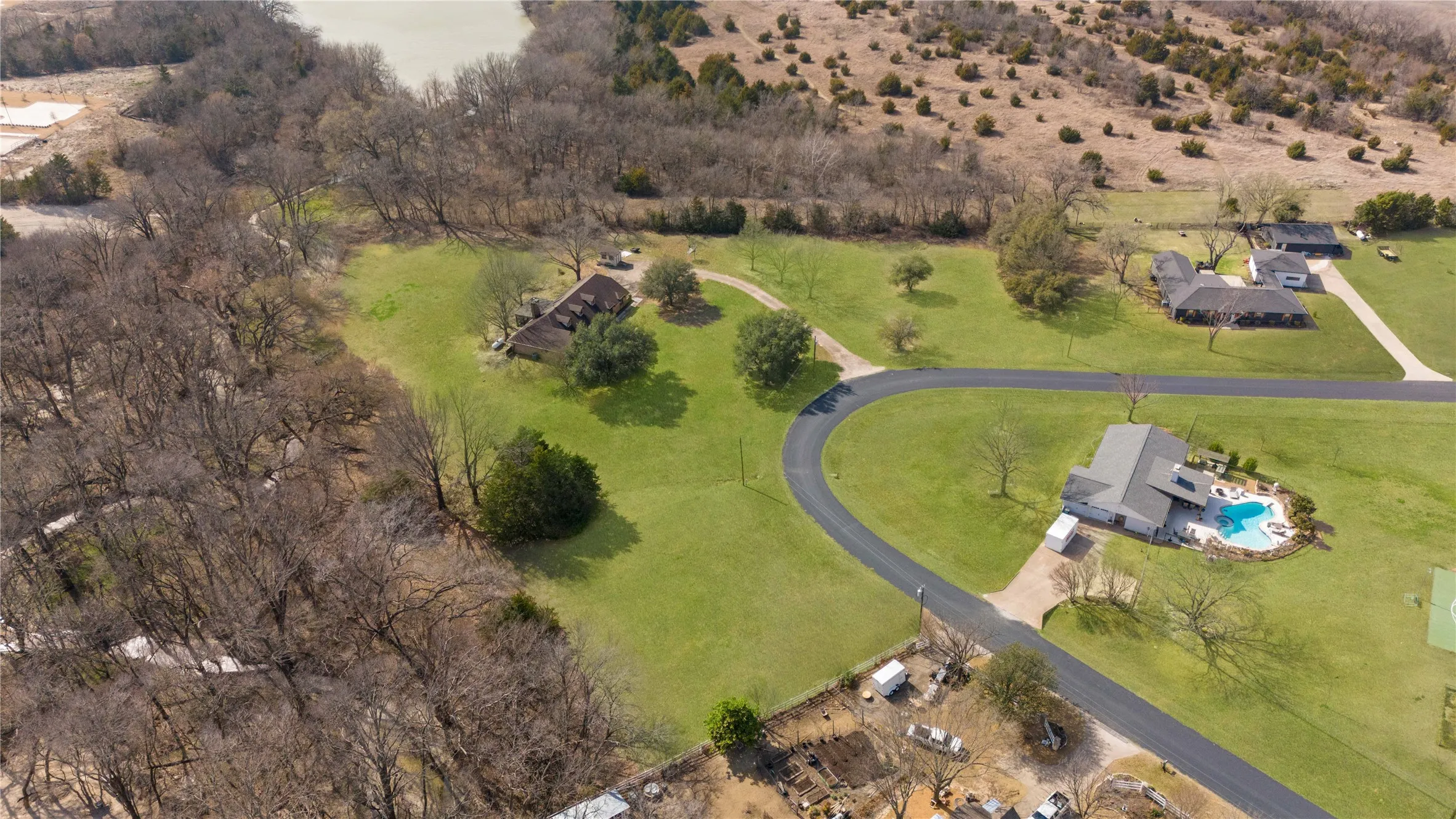 Extensive property featuring a manicured lawn, a winding paved driveway, a private swimming pool, mature trees, and direct water access