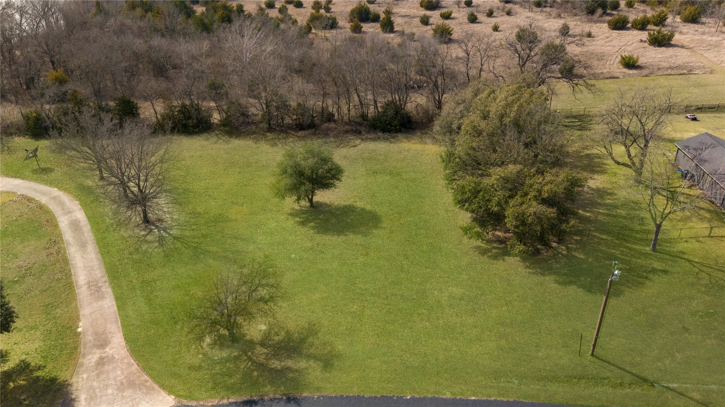 Expansive green acreage featuring a curved paved driveway, mature trees, and a distant treeline