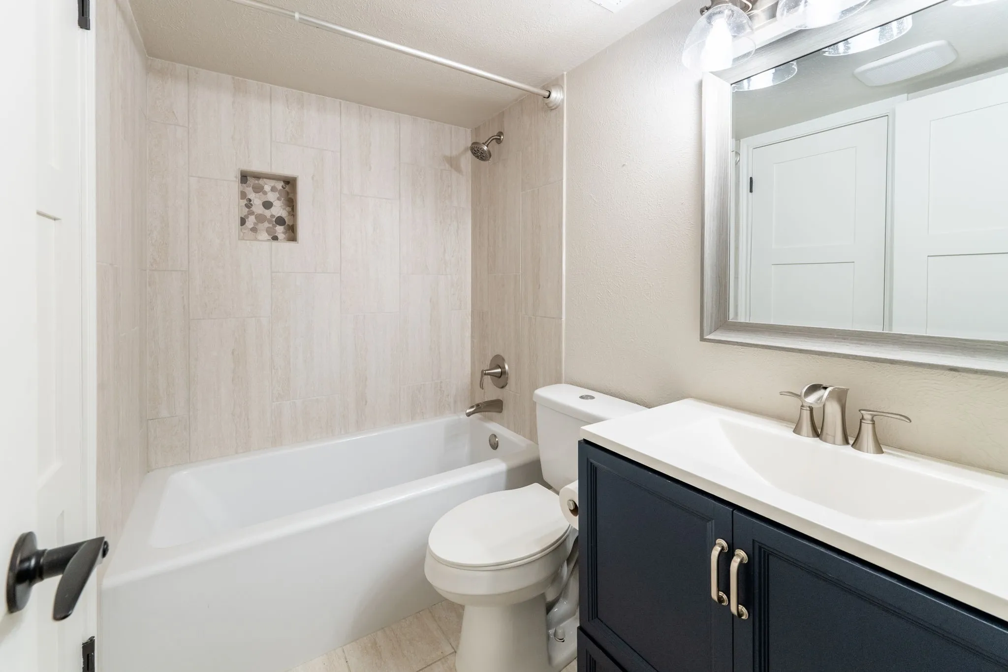 Bathroom featuring a shower-over-tub combination with light-toned tile surround and a recessed niche