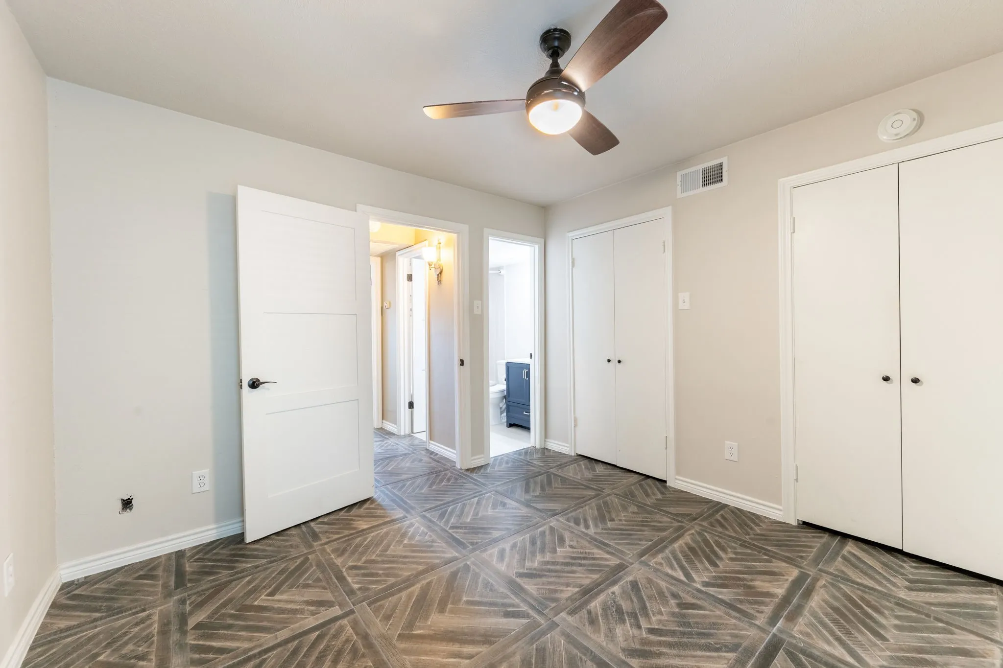 Room featuring a ceiling fan with integrated lighting, wood-finish flooring with a geometric pattern, and neutral-toned walls