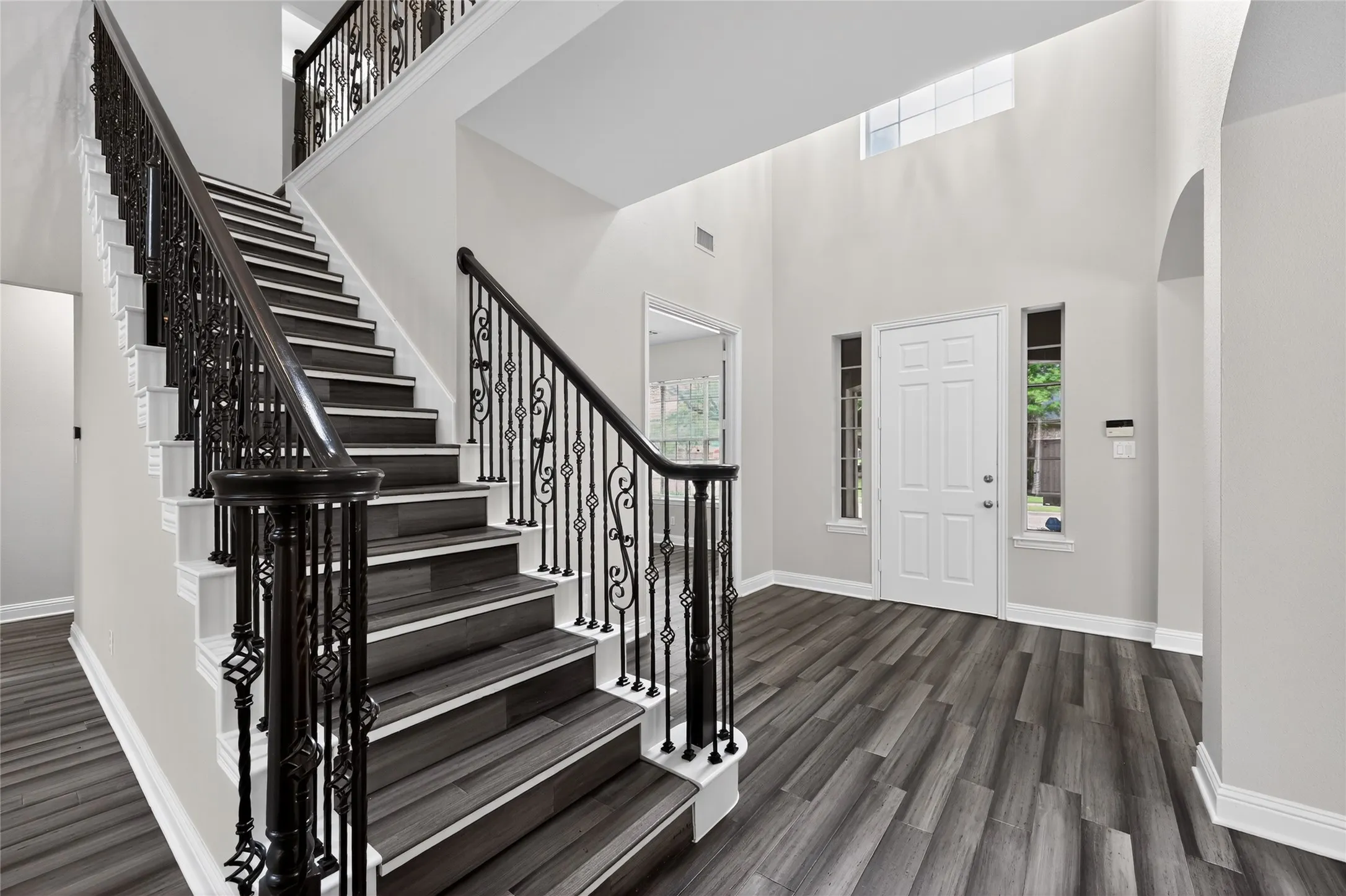 Two-story entryway featuring a grand staircase with wrought iron balusters and dark wood-finish flooring