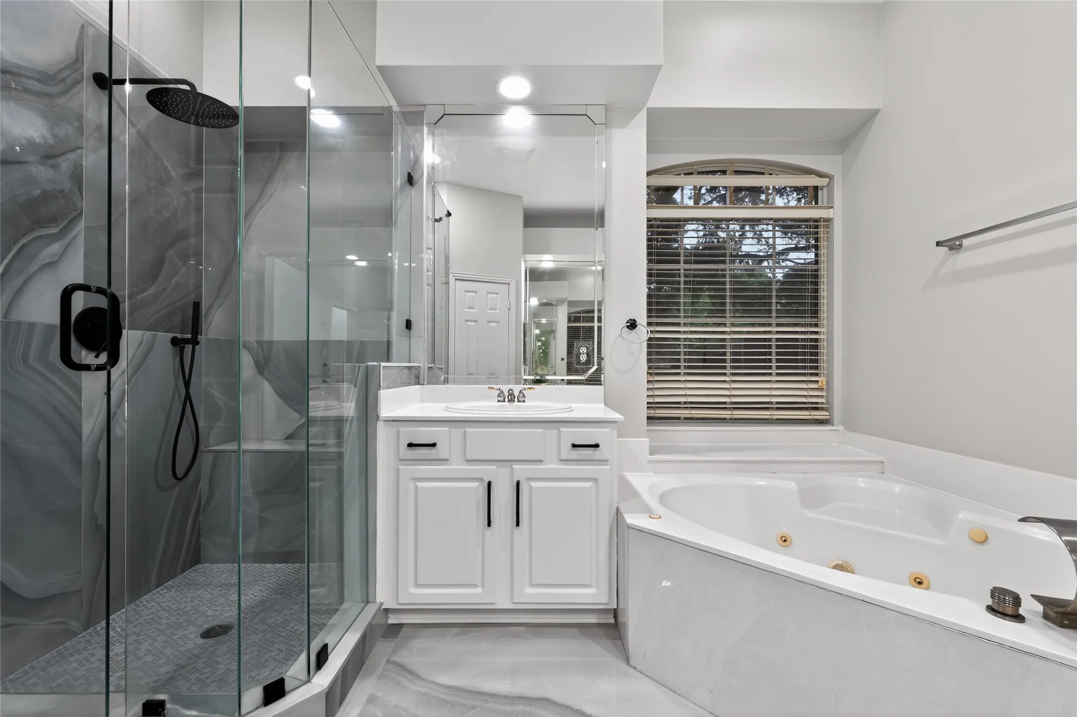 Modern primary bathroom featuring a glass-enclosed shower with dark-toned fixtures and a rainfall showerhead