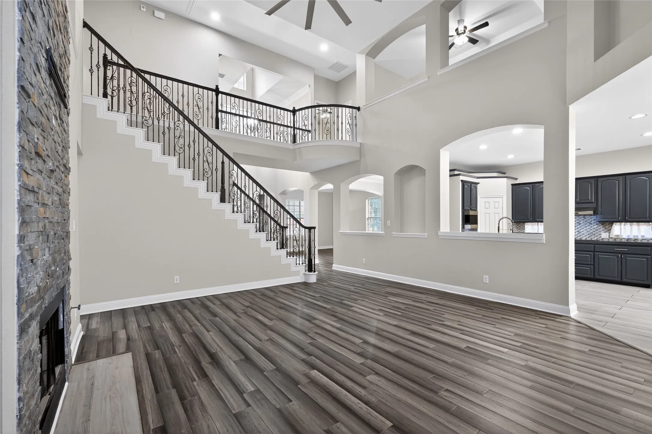 Two-story living area featuring wood-finish flooring, a stone-clad fireplace, and an ornate wrought iron staircase