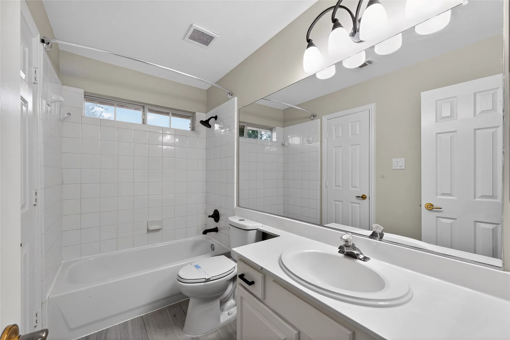 Connecting bathroom between bedroom #2 and bedroom#3 featuring a white vanity with an integrated sink, a large wall-mounted mirror, and a tub/shower combination with white tile surround